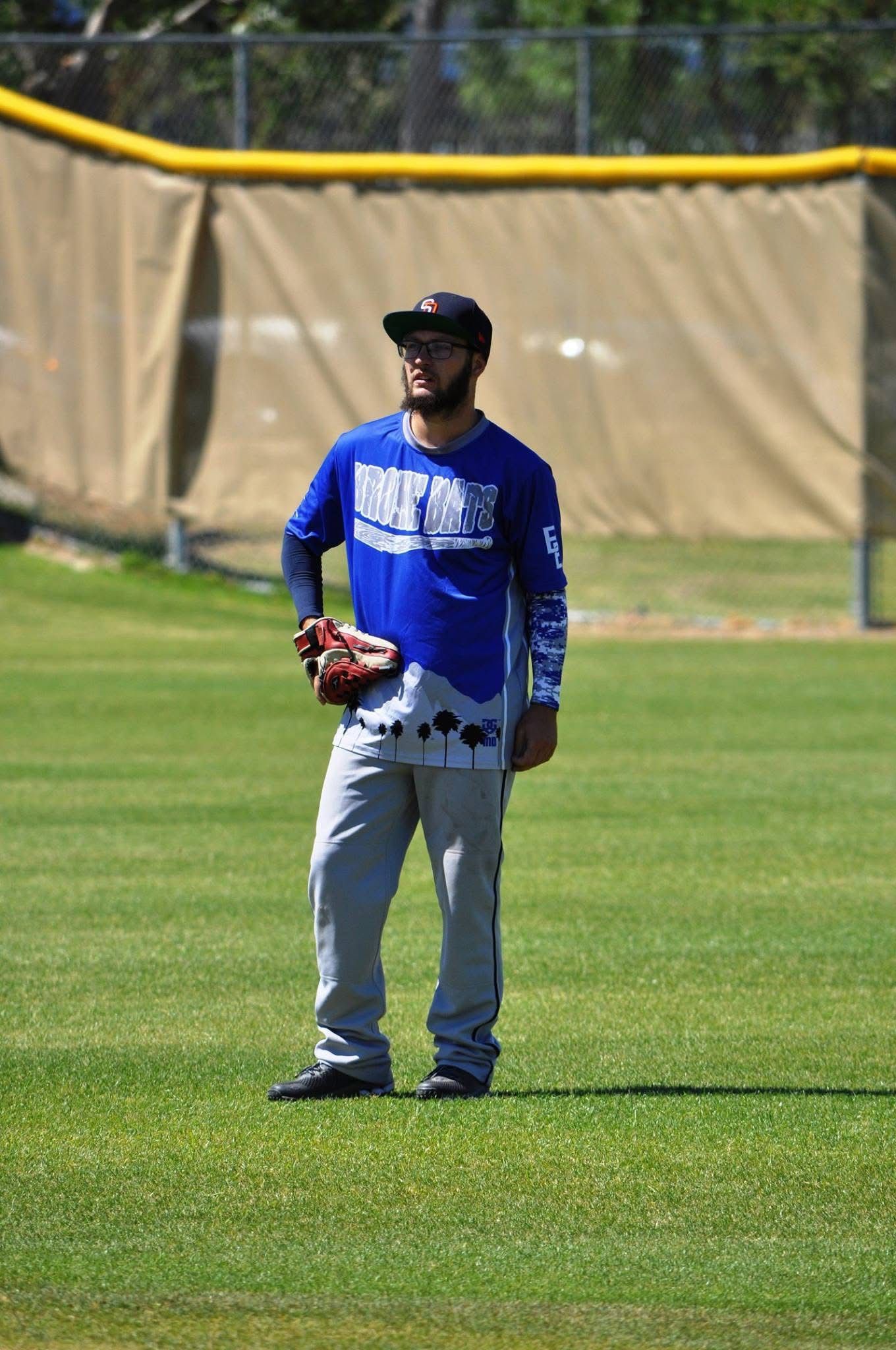 Baseball player in blue jersey and gray pants standing on a grass field with a glove in hand