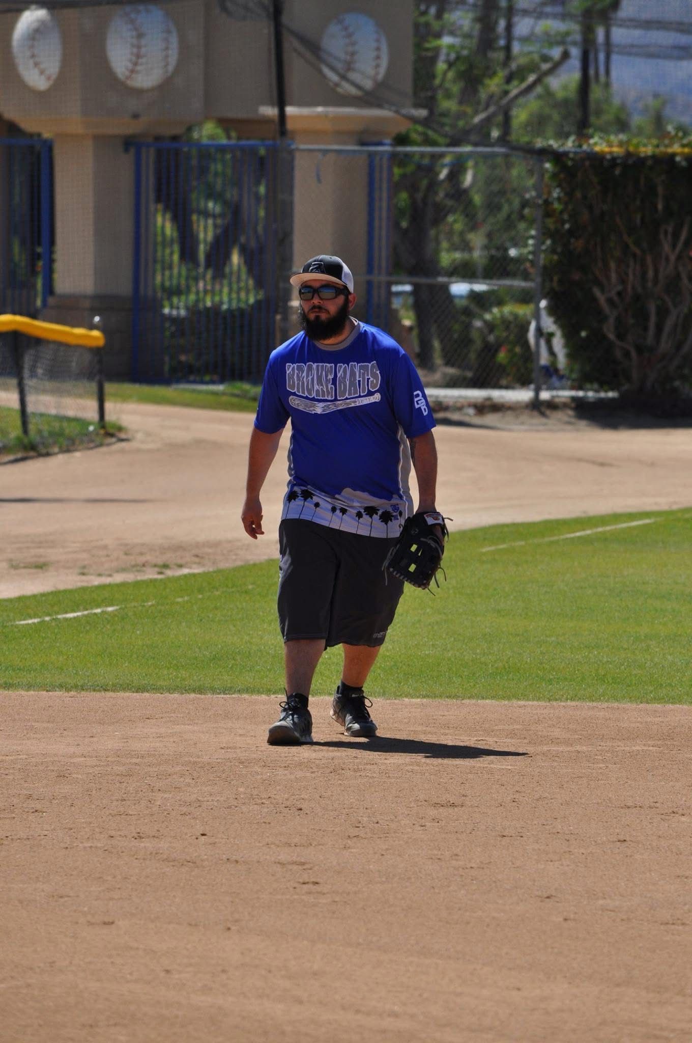 Person in a blue shirt and black shorts standing on a baseball field with a glove in hand.