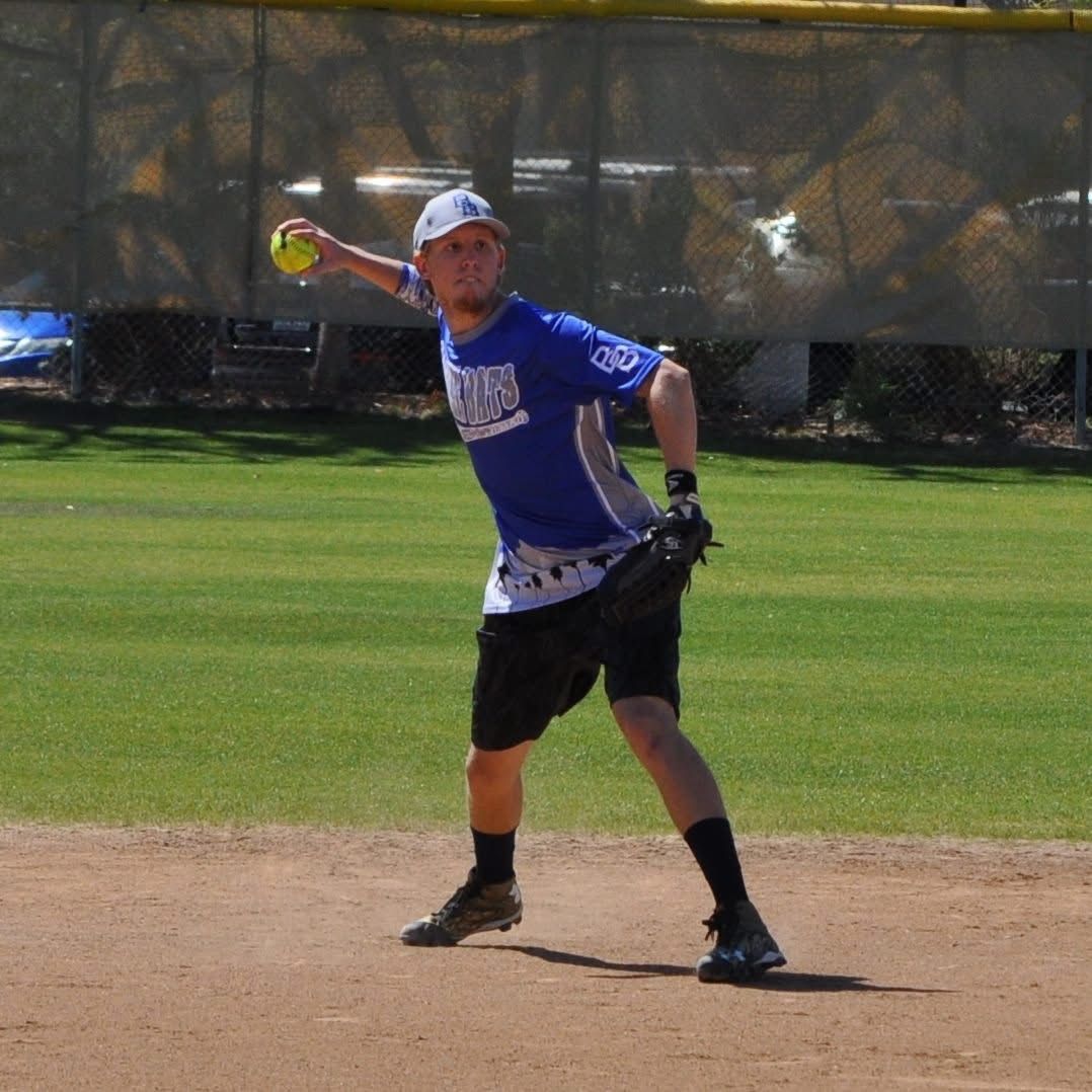 Softball player in blue jersey and black shorts mid-throw on a dirt infield.
