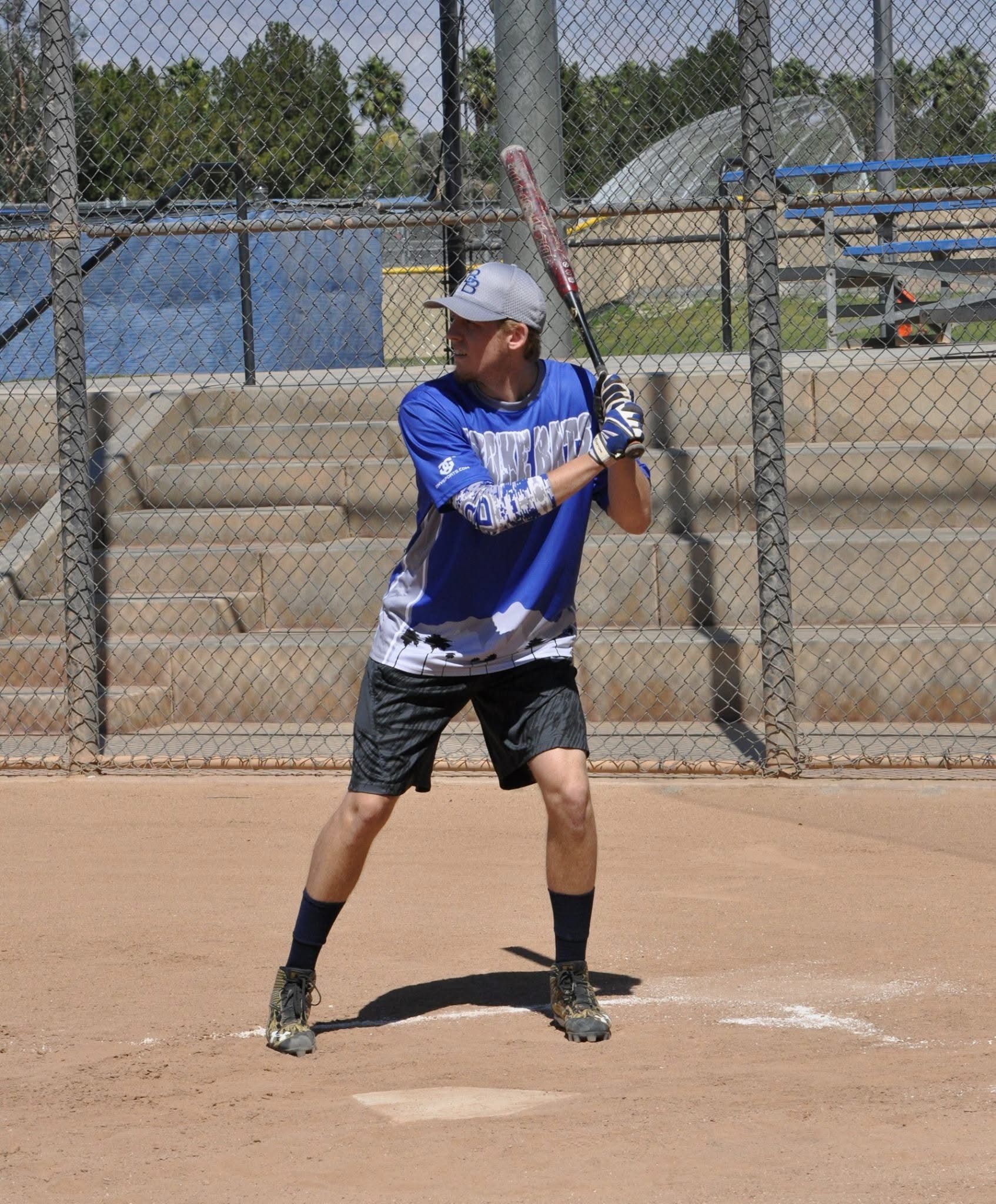 Baseball player in blue jersey and white cap at bat on a dirt field, ready to swing.
