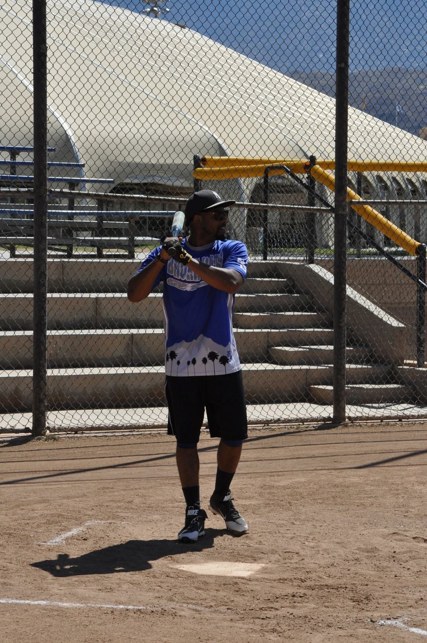 Baseball player in blue jersey standing at home plate with bat, ready to hit on a sunny field.