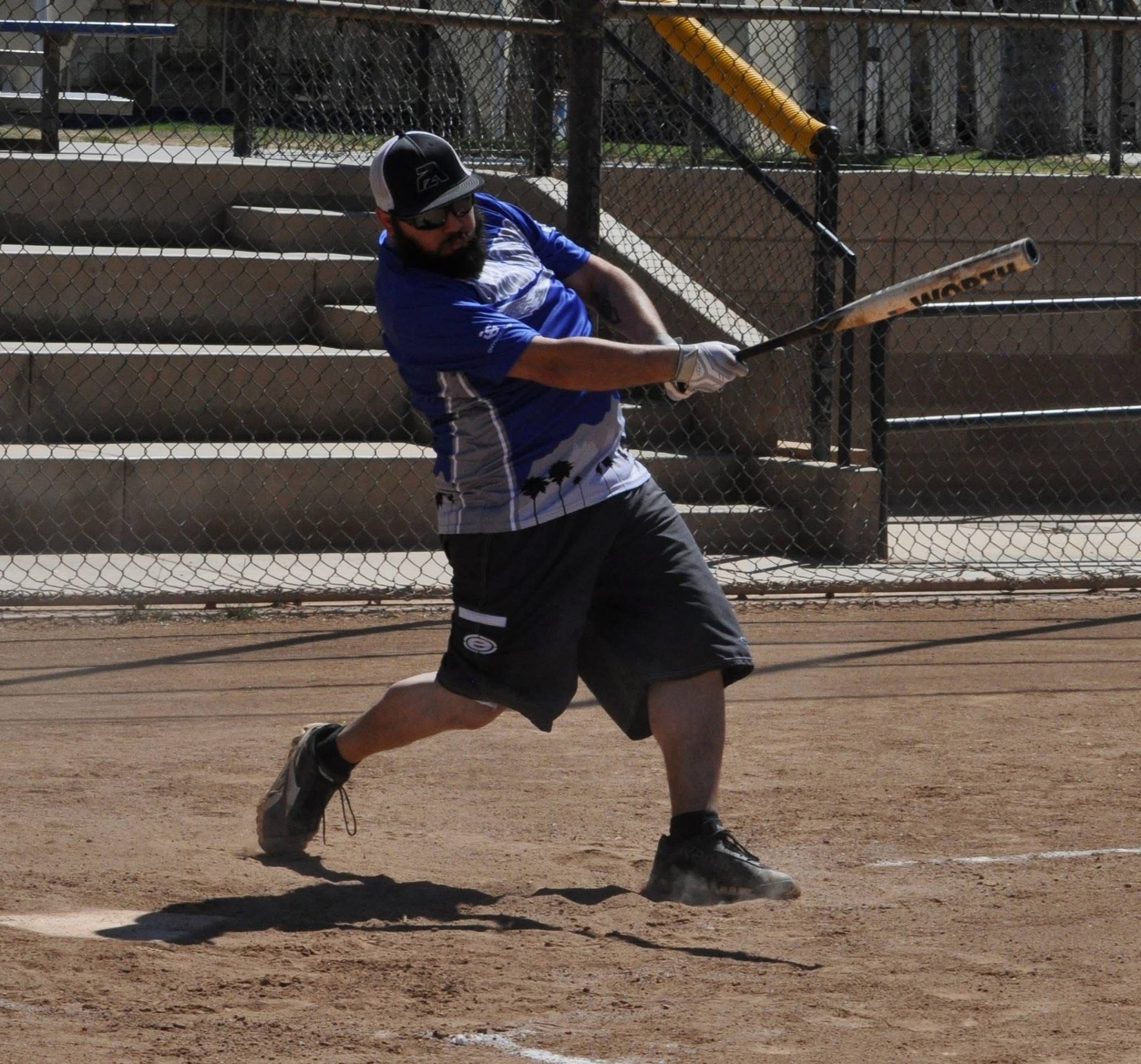 Baseball batter in blue jersey swinging a bat on a dirt field, with bleachers in the background