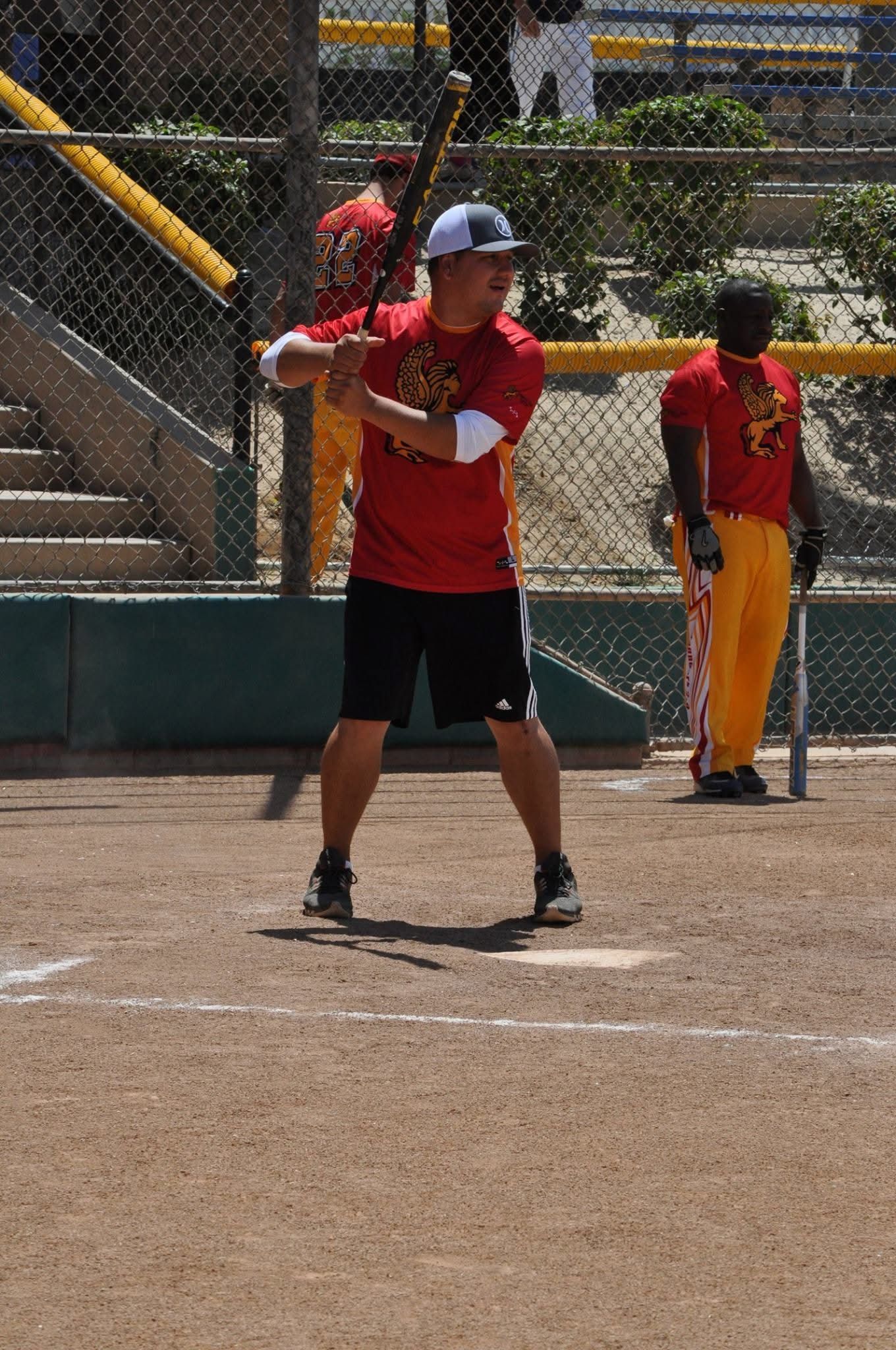 Baseball batter in red shirt and black shorts preparing to swing at a ball on a dirt field