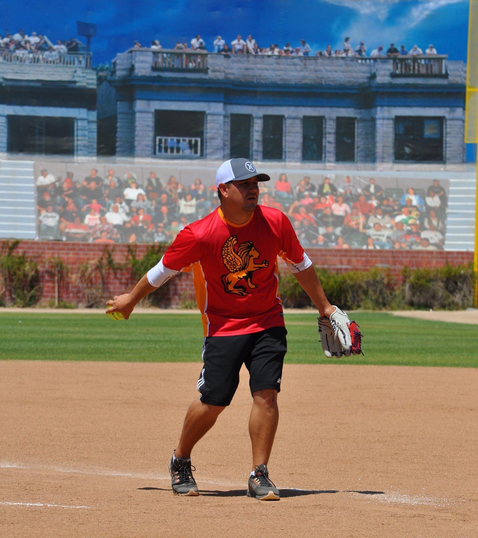 Baseball player in red shirt and black shorts standing on the infield, holding a glove on a sunny field
