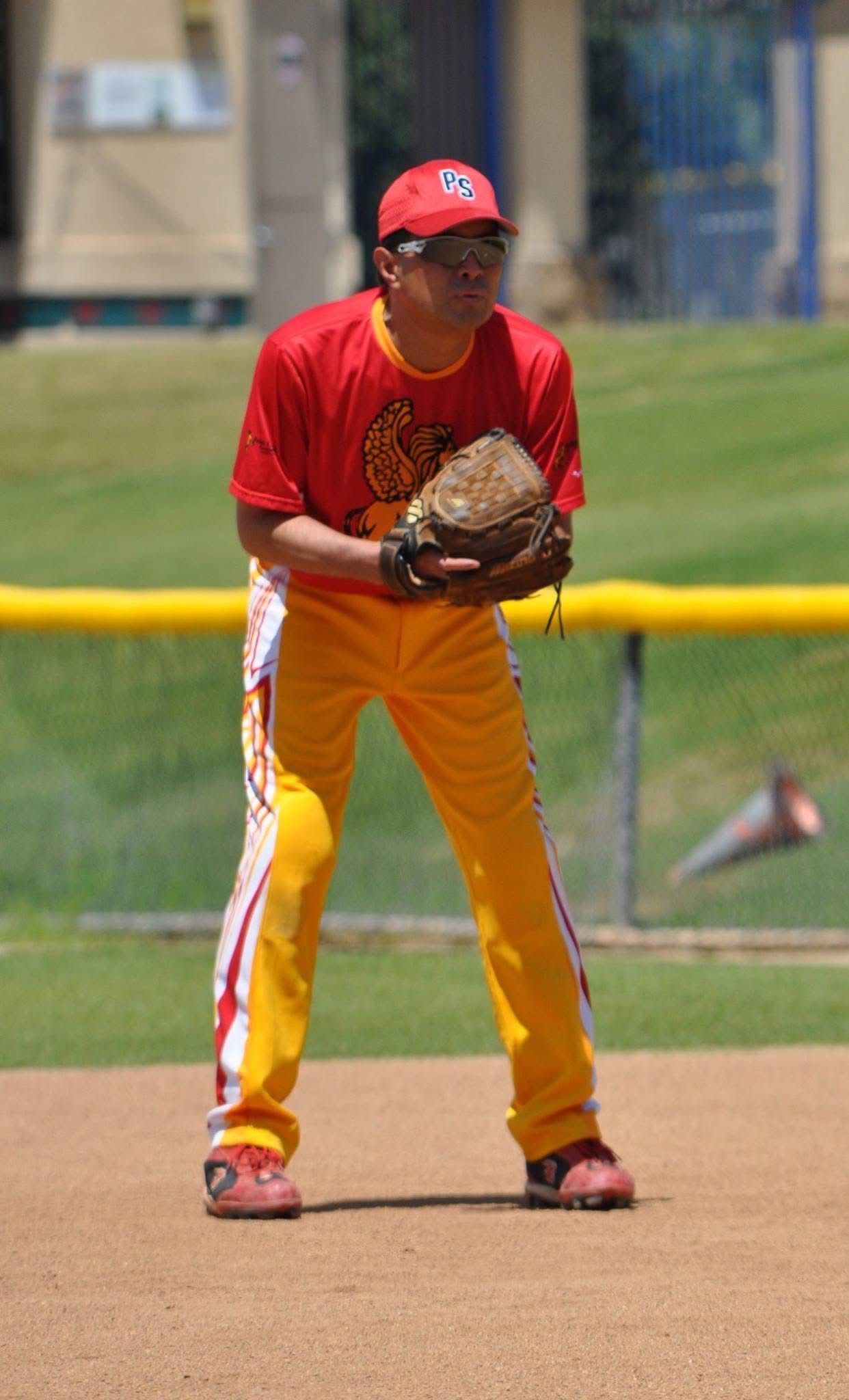 Baseball player in red and yellow uniform crouches ready on the field with glove up