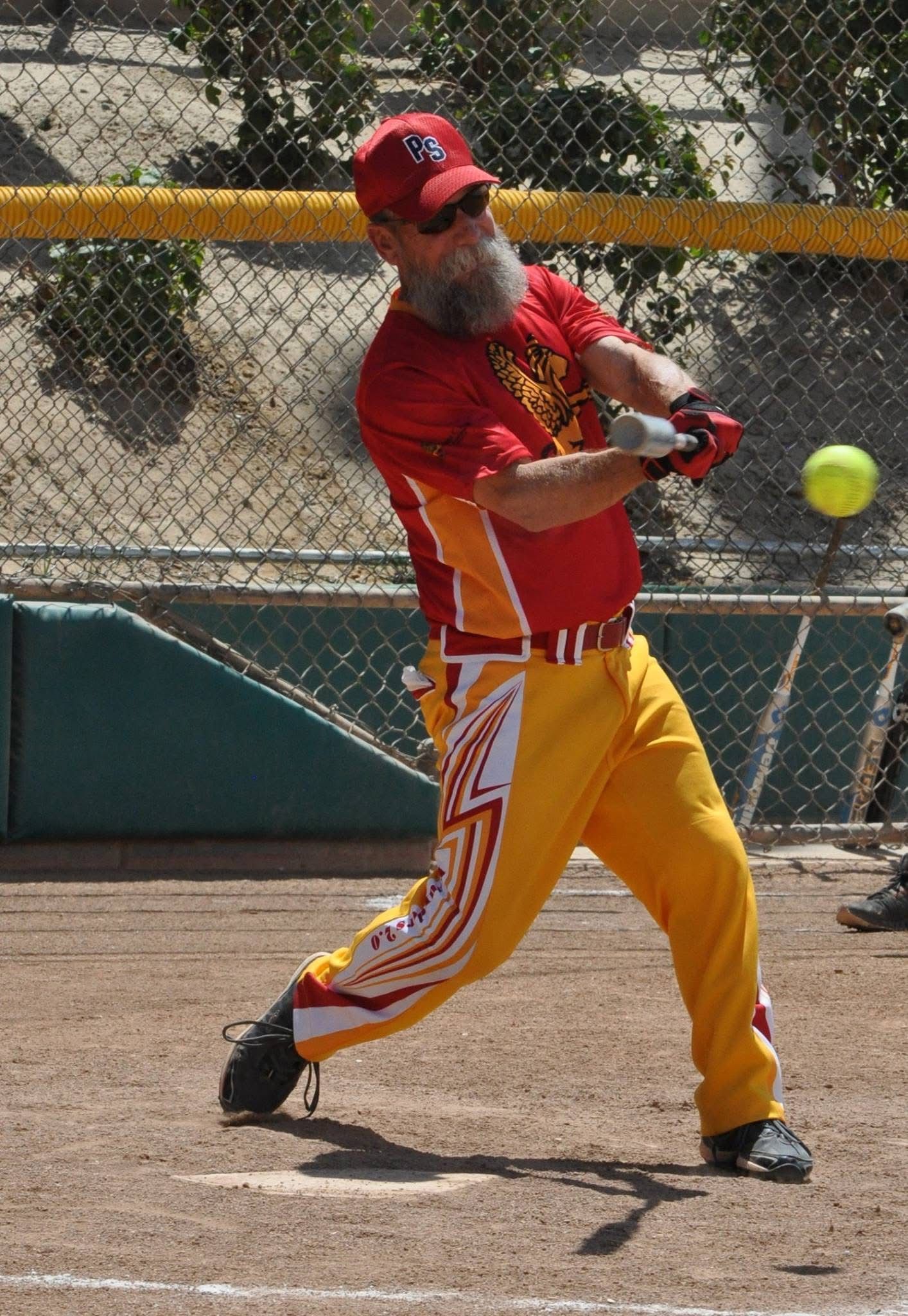 Baseball player in red and yellow uniform swinging at a pitch on a dirt field