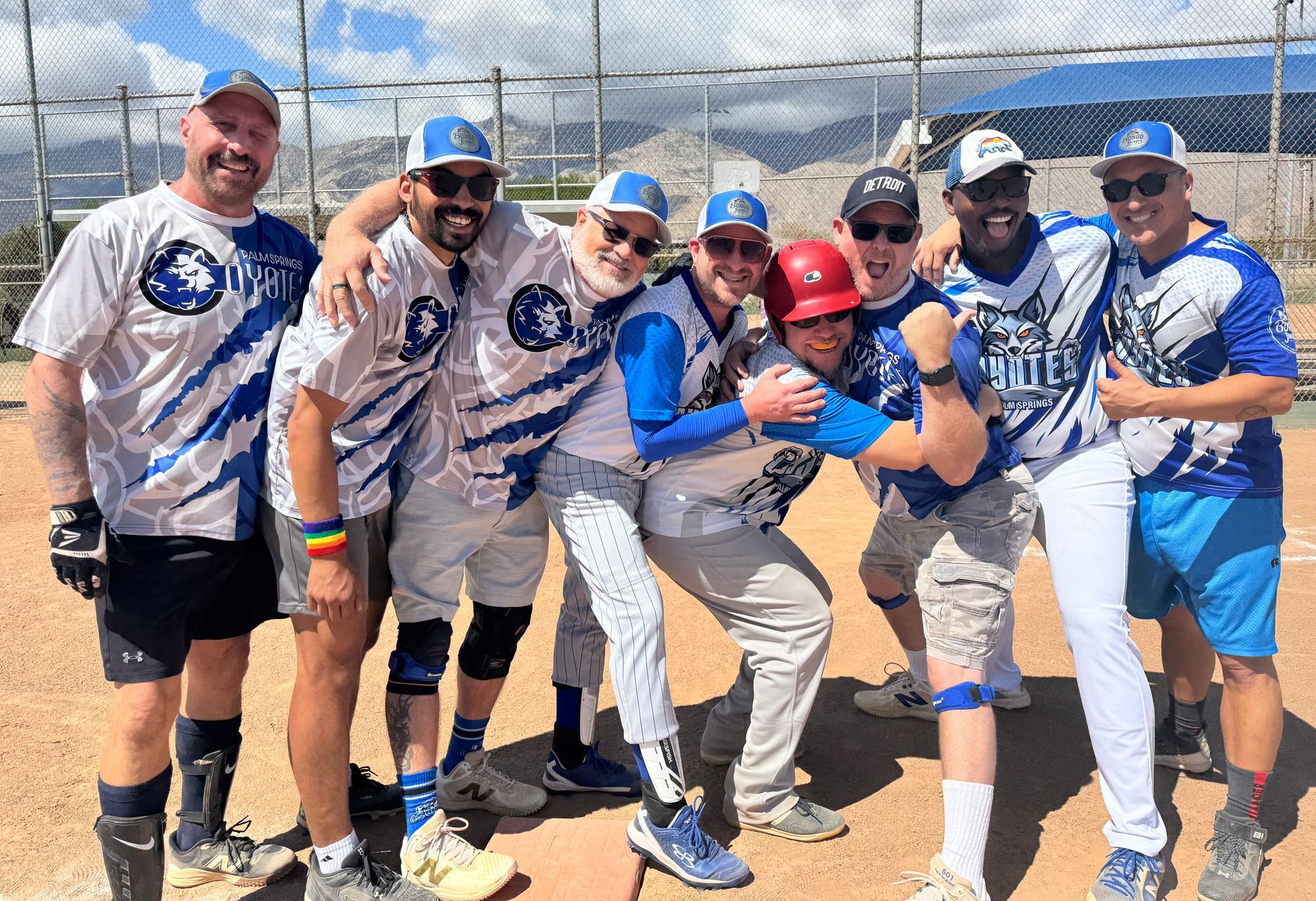 Group of softball players in blue-and-white uniforms posing together on a sunny field, holding a ball and smiling