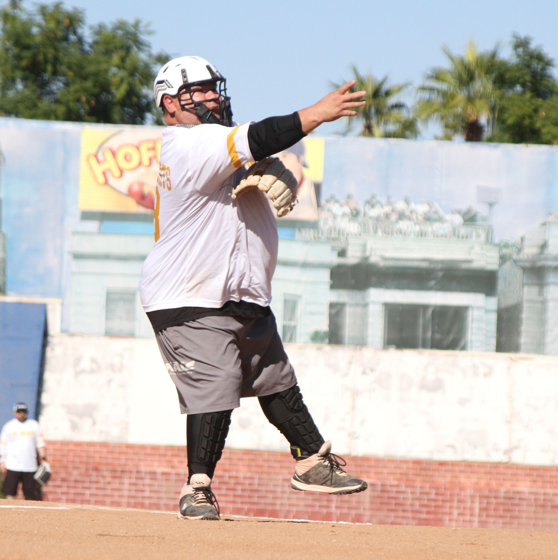Athlete in white helmet and jersey throwing a ball on a field outdoors