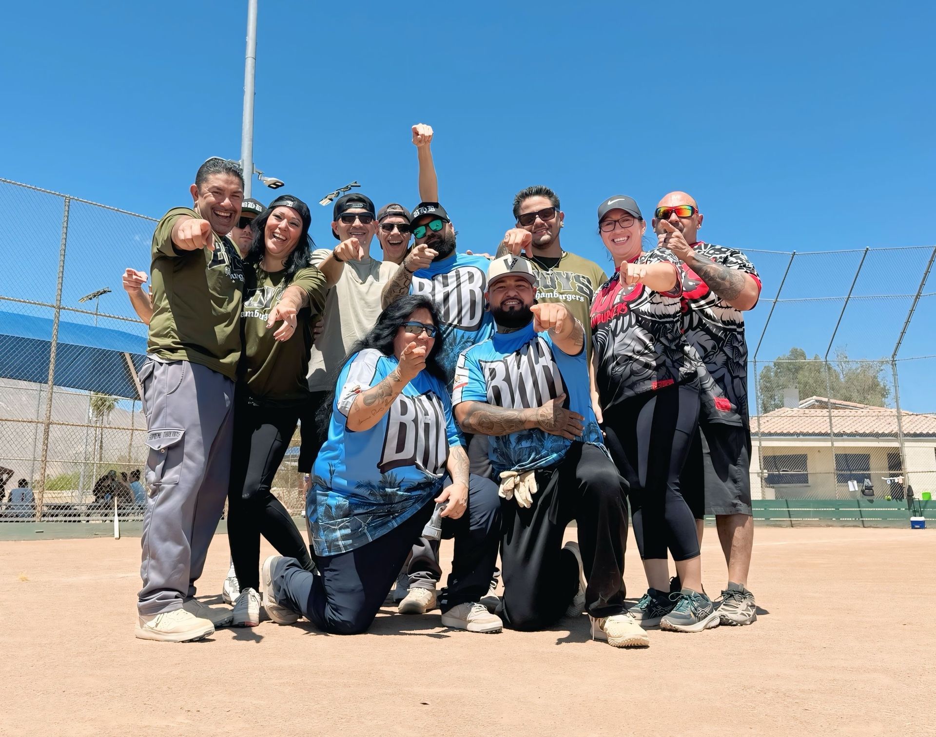 Group of people posing and cheering on a softball field under a bright blue sky