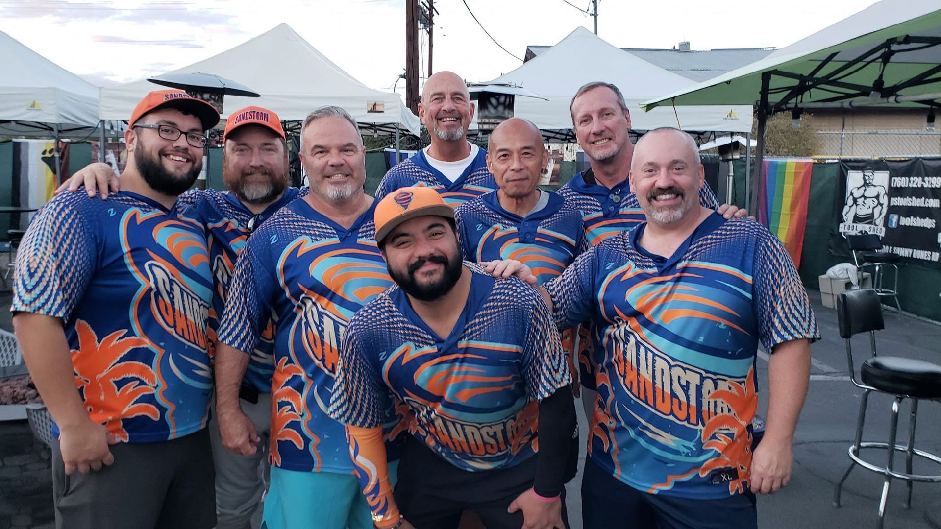 Group of people in matching blue-orange shirts posing together outdoors at an event.