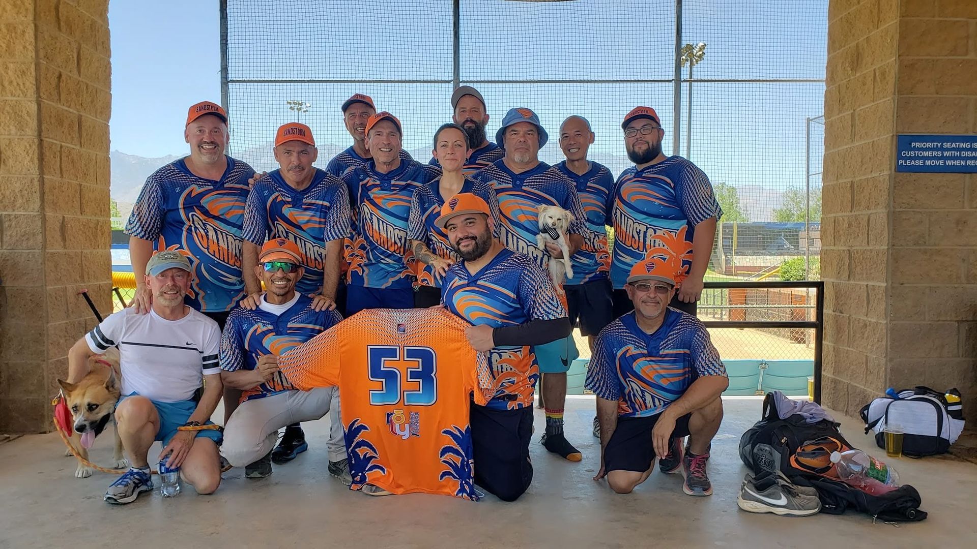 Youth baseball team in blue and orange uniforms posing for a group photo under a pavilion