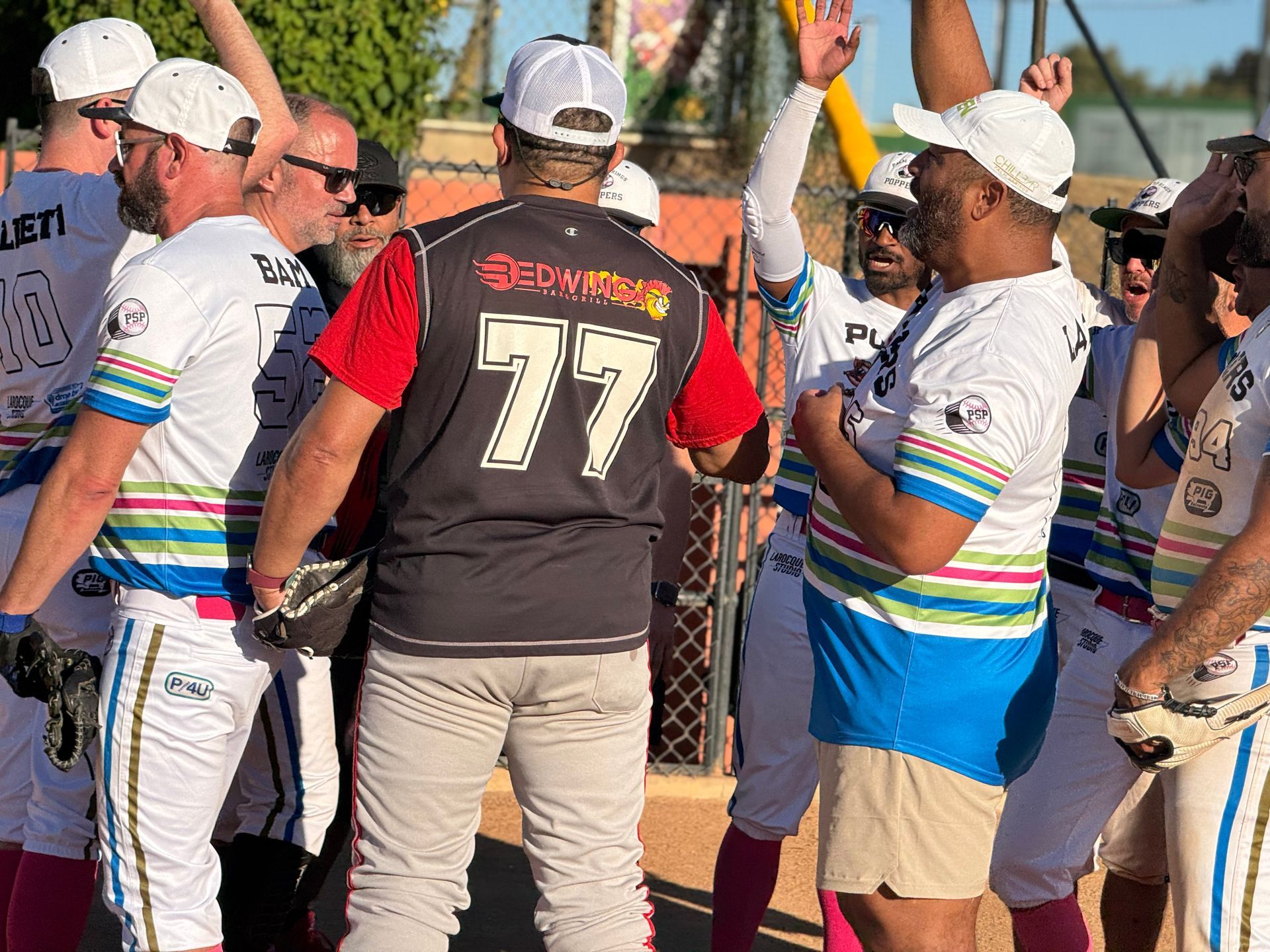 Baseball coaches and players huddle near the dugout, one coach raising a hand on the field side.