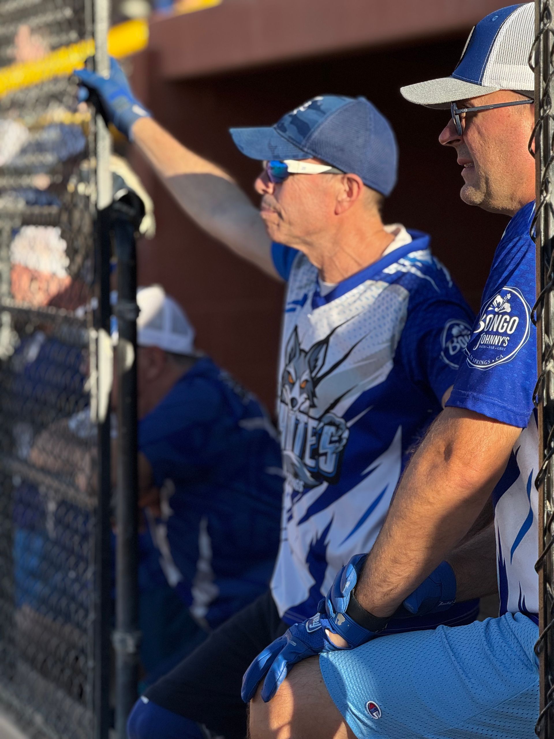 Baseball fans in blue jerseys cheering from the dugout behind a chain-link fence