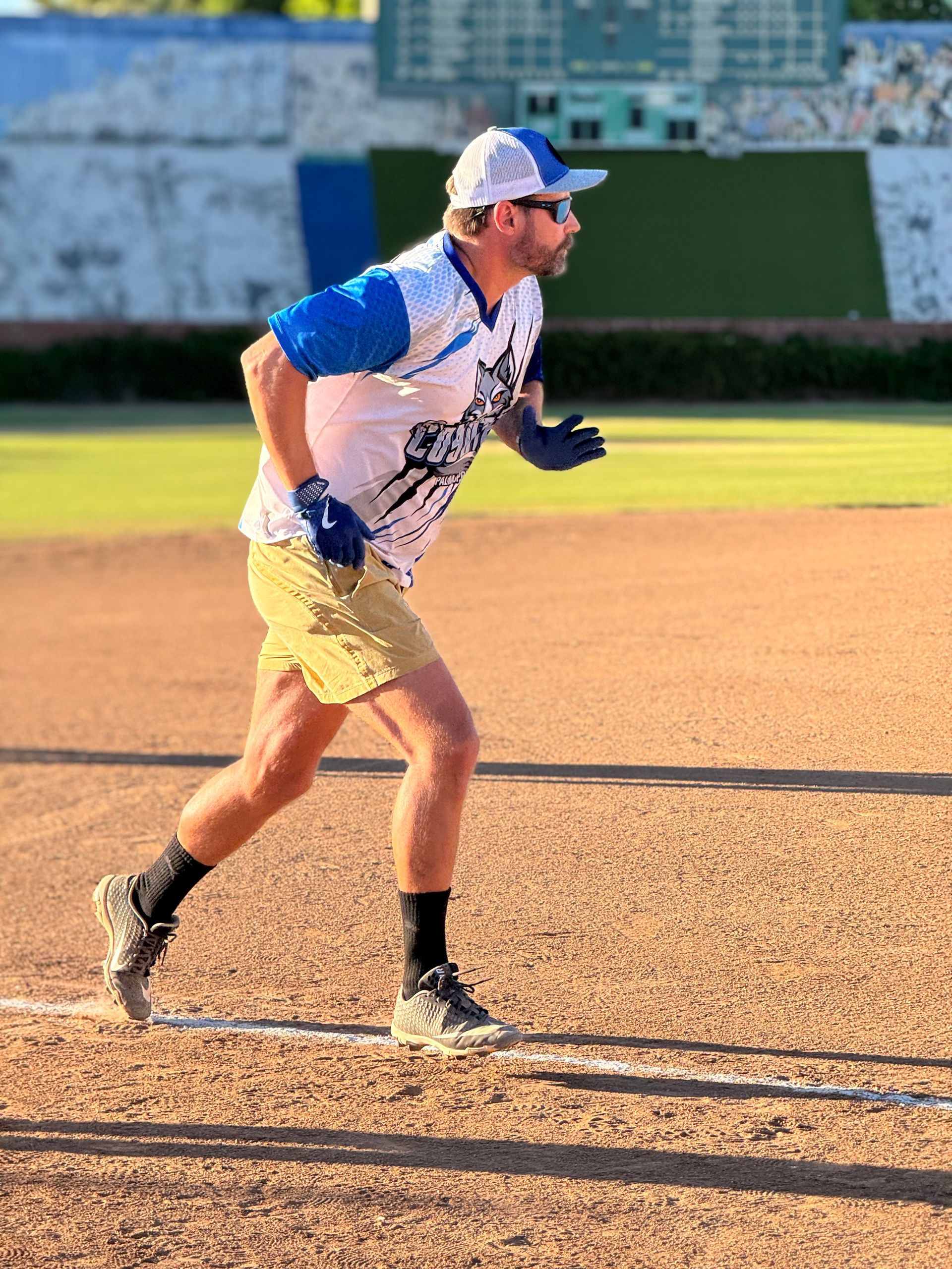 Baseball player in a white and blue uniform running on a dirt field in bright sunlight