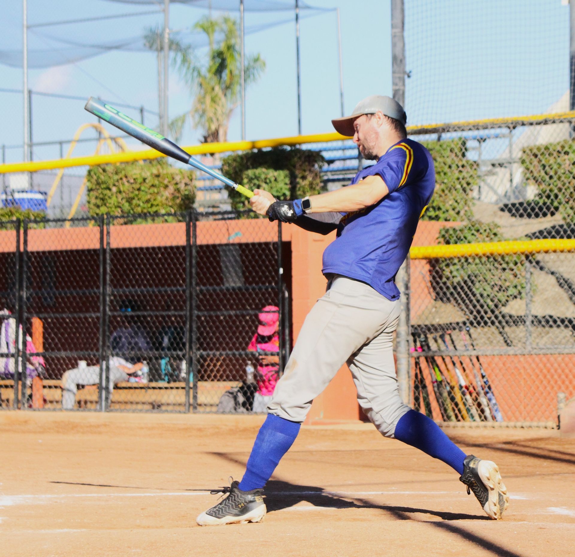 Baseball player in blue swings a bat at a sunny outdoor field.
