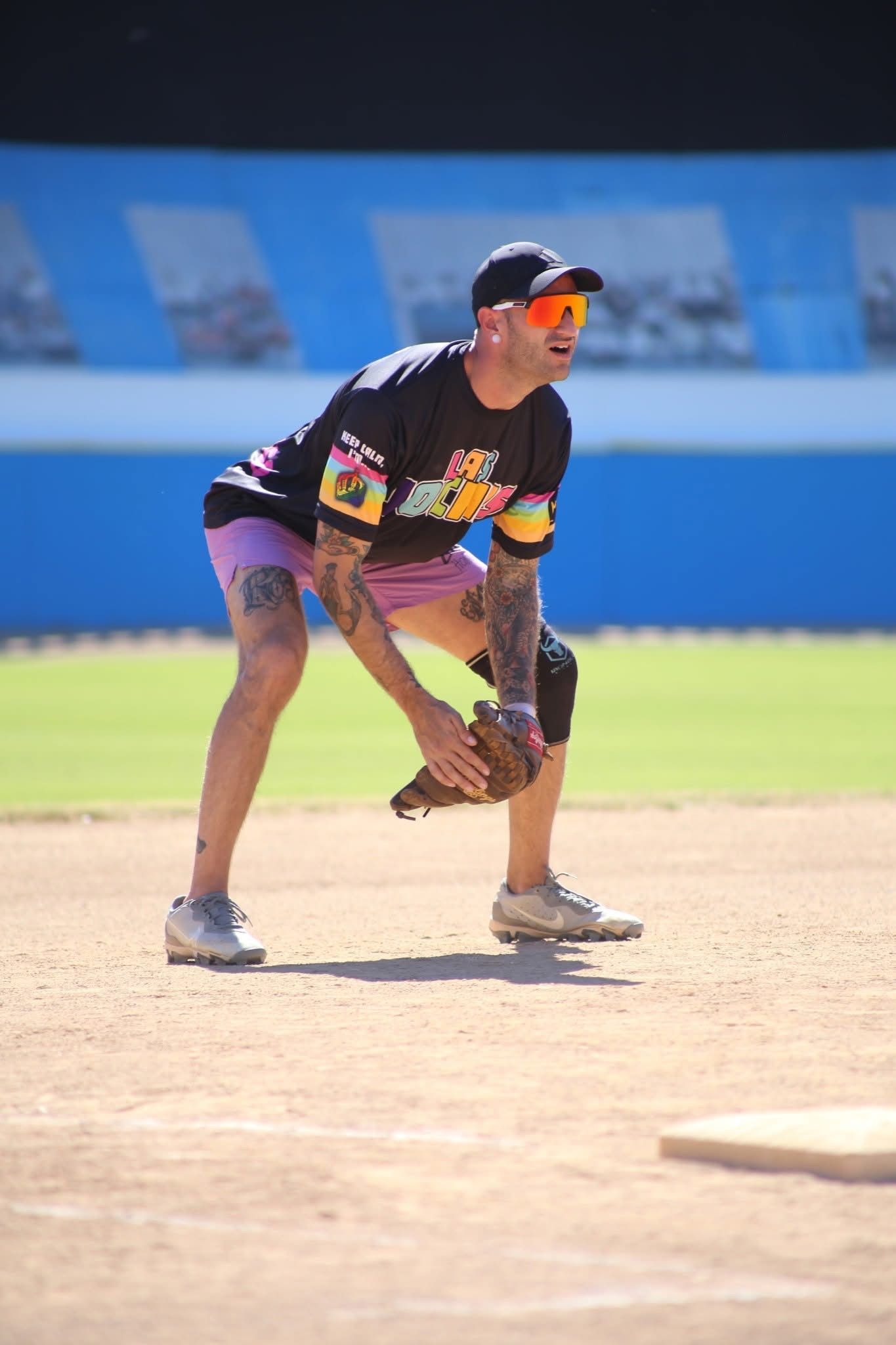 Baseball player in black uniform crouching on a sunlit infield, ready for play