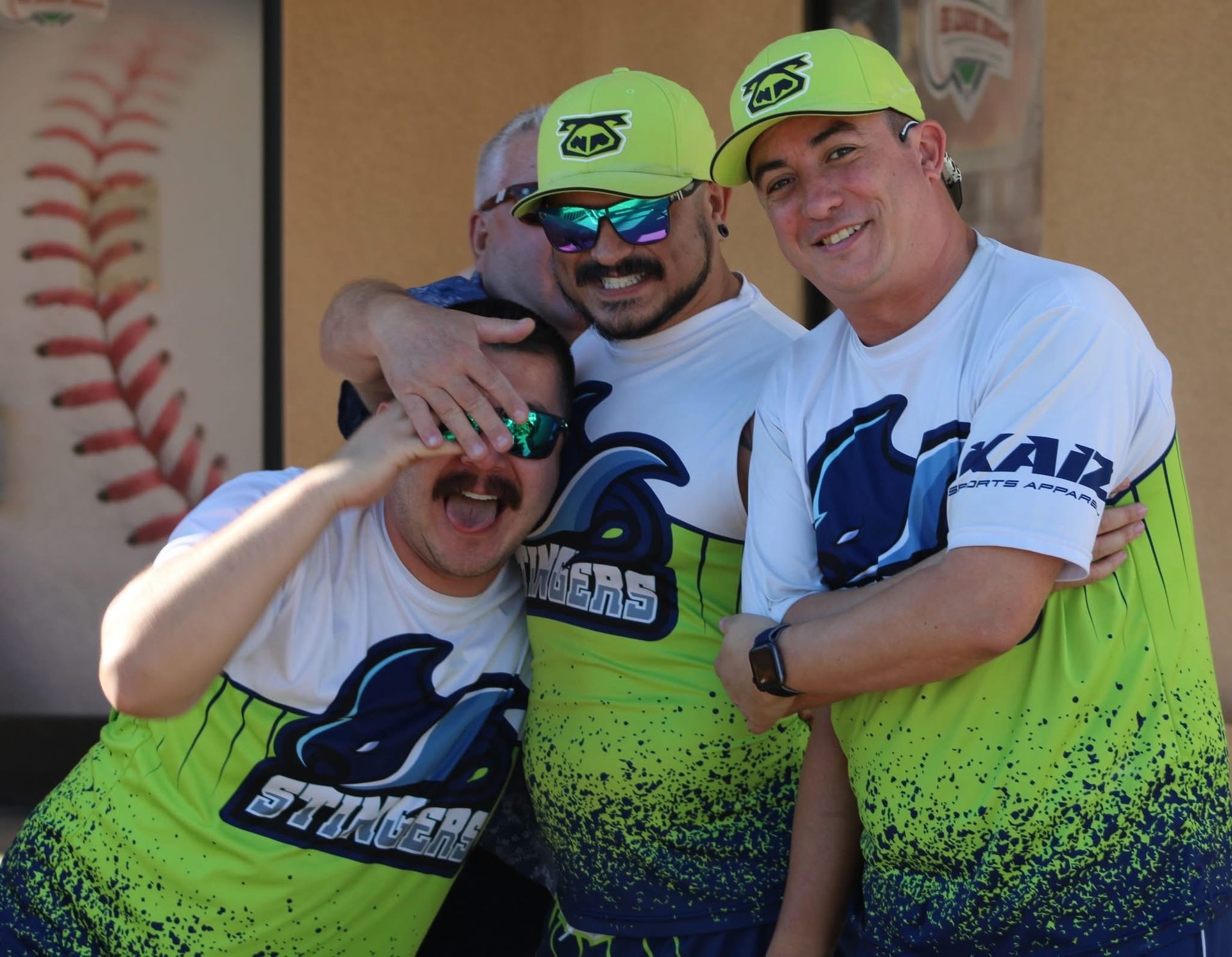 Three smiling baseball players in neon caps and jerseys posing together outdoors.