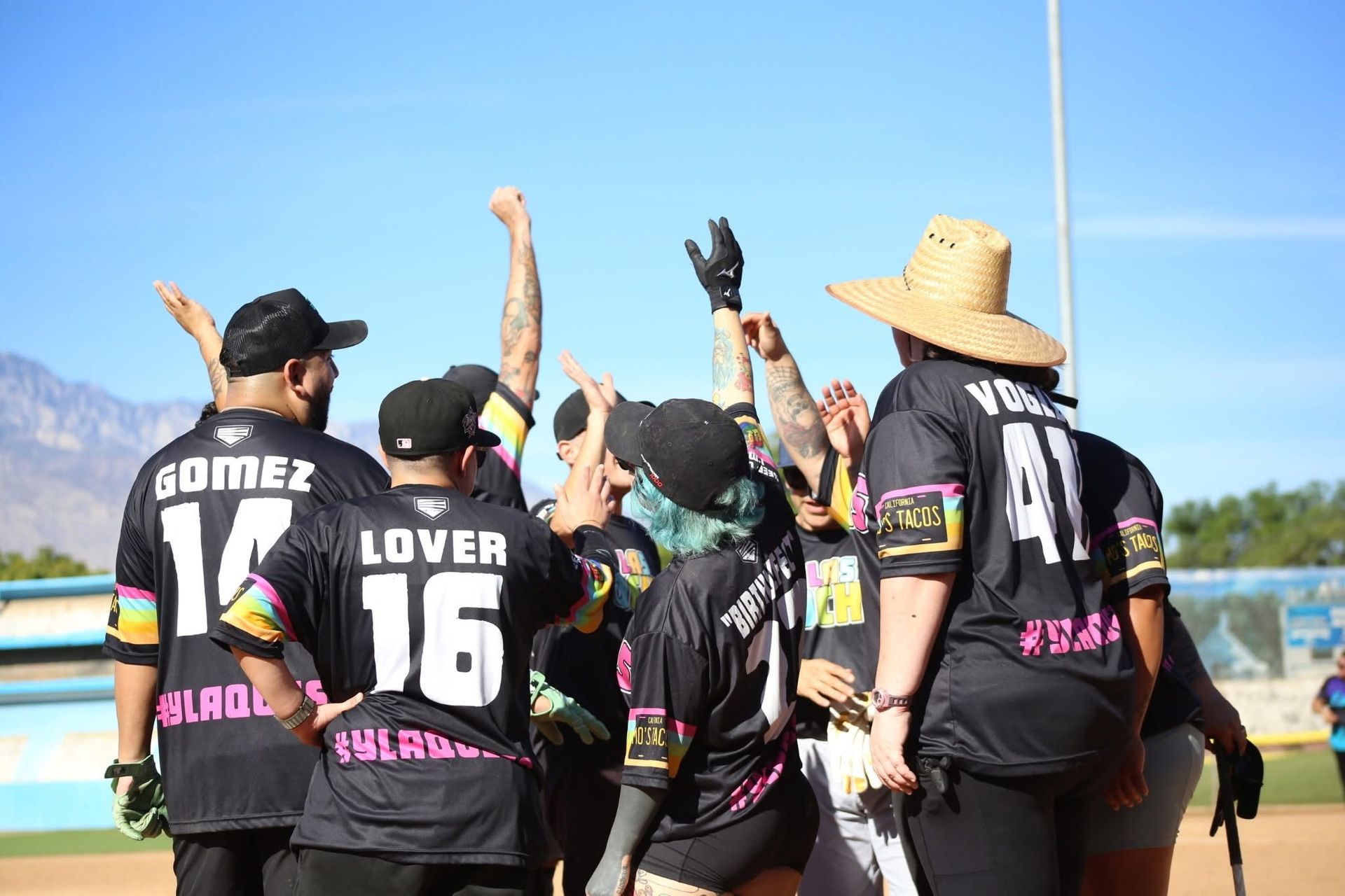 Baseball team in black jerseys celebrating on the field with arms raised under a bright sky