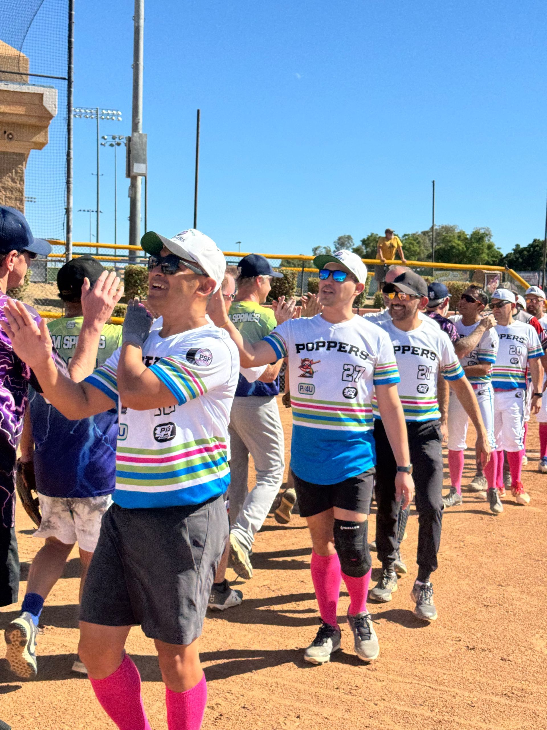 People in white striped shirts and hats marching in a sunny outdoor parade or walk