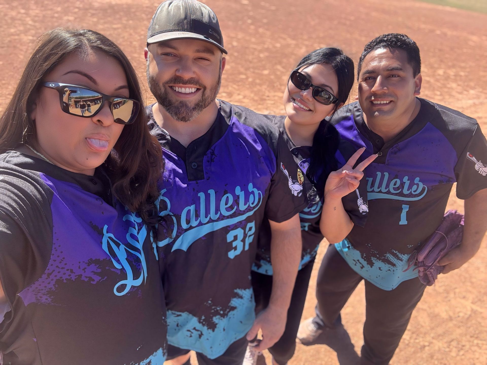 Four people in matching purple and black shirts posing outdoors in bright sunlight