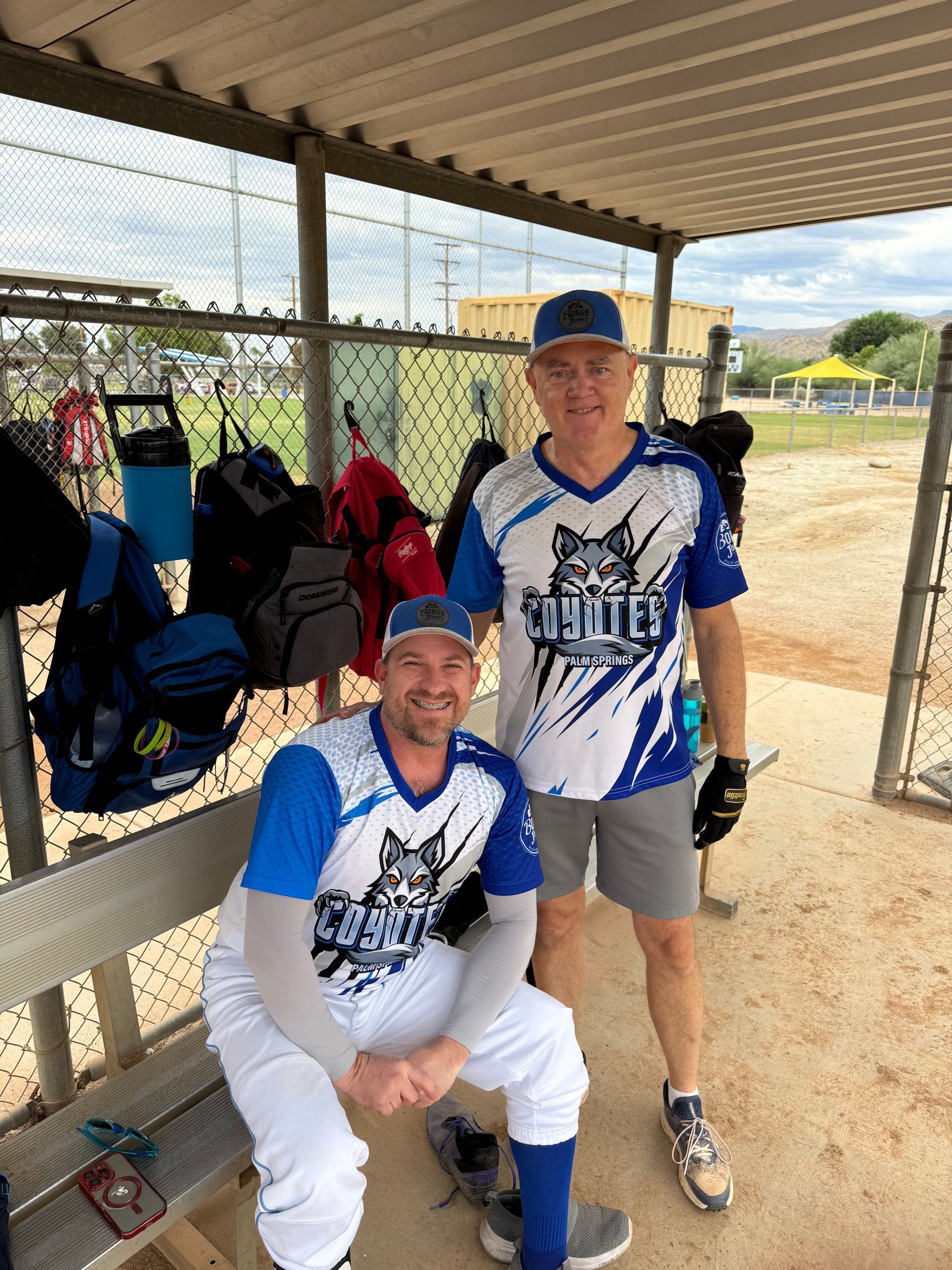 Two people in blue and white sports uniforms posing under a dugout at a baseball field