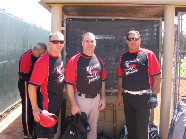 Three baseball players in red-and-black uniforms standing in a dugout, one holding a cap.