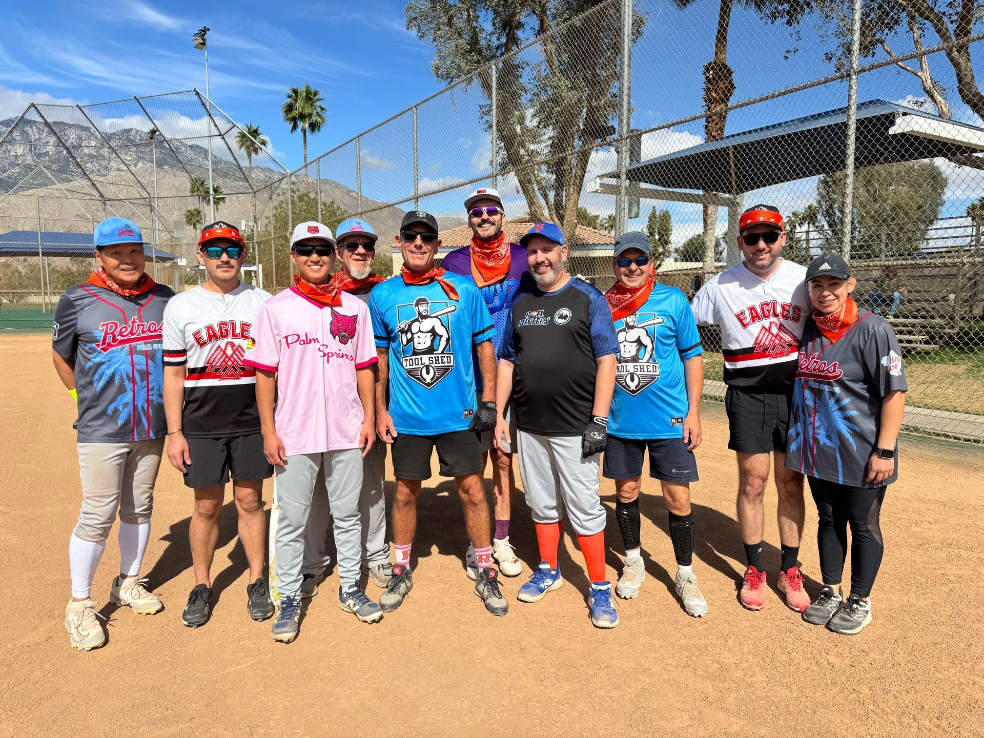 Group of softball players posing on a field in colorful jerseys and caps under a sunny sky