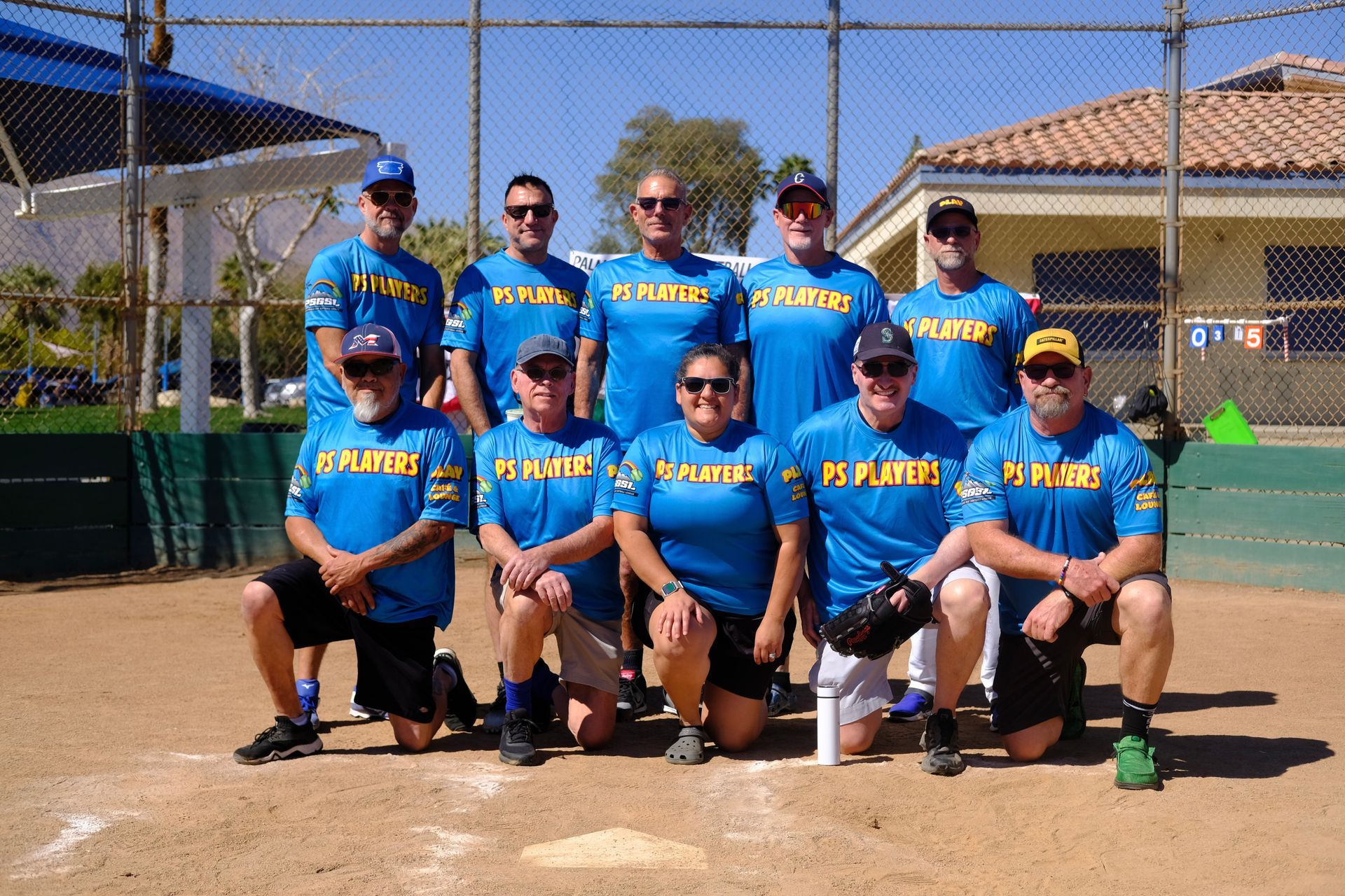 Youth softball team in blue jerseys posing on a baseball field with bats and gloves