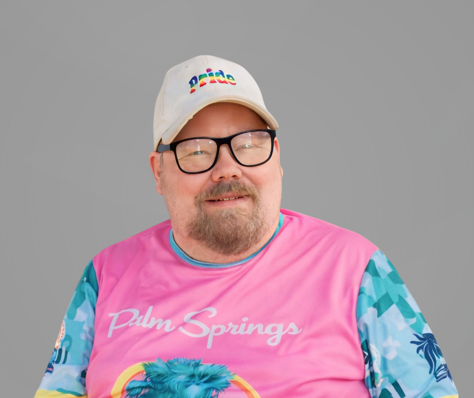 Headshot of Brian Thompson, a man smiling, wearing a pair of glasses, a baseball cap and jersey, set upon a gray background.