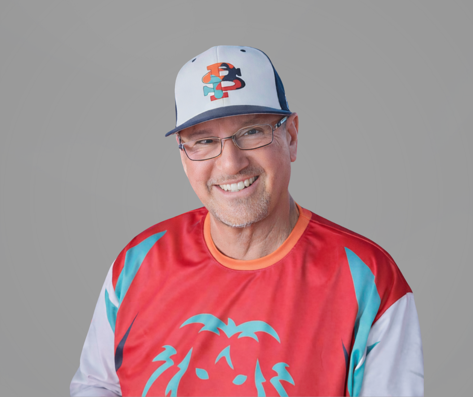 Smiling man in a gray cap and glasses wearing a red-and-teal shirt against a gray background