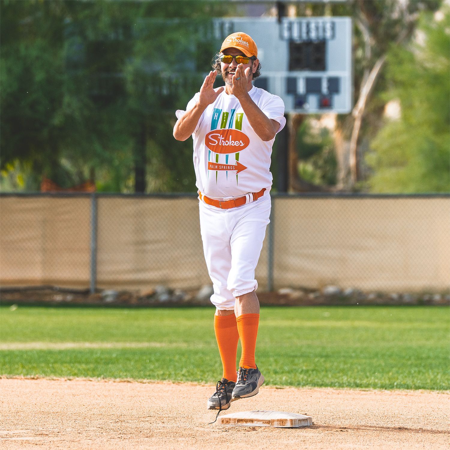 Baseball player in white uniform claps near first base on a sunny field