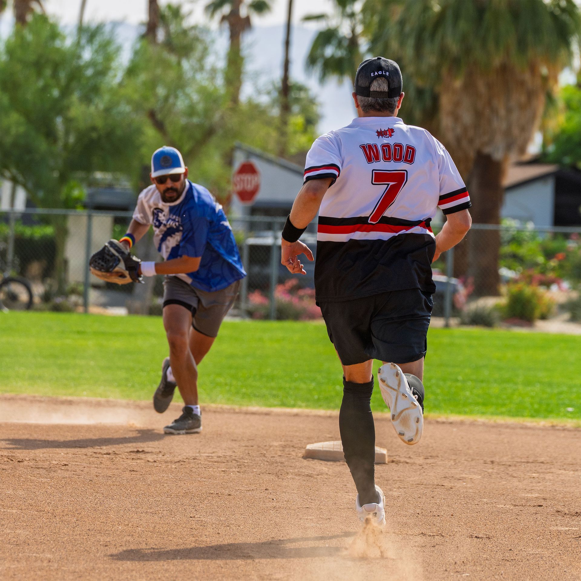 Two softball players sprinting between bases on a sunny field, one reaching for the ball
