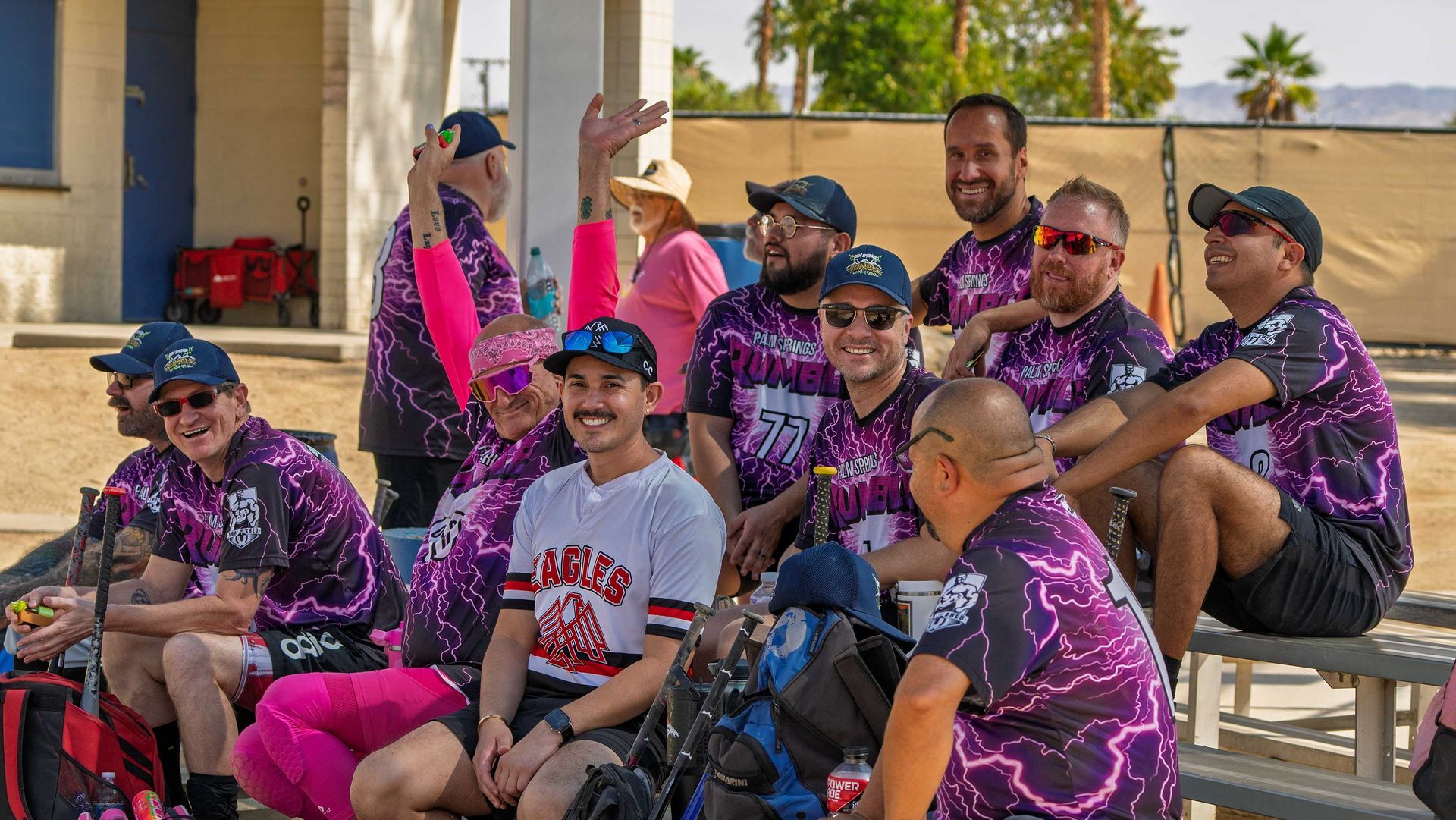 Group of people in purple team jerseys sitting outdoors on bleachers, smiling and chatting.