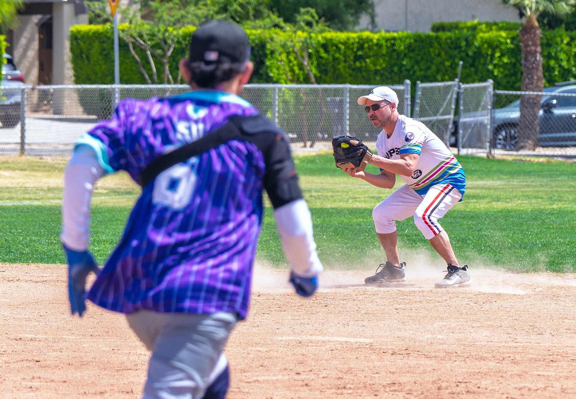 Two softball players on a dusty field, one fielding a ball while another runs toward base