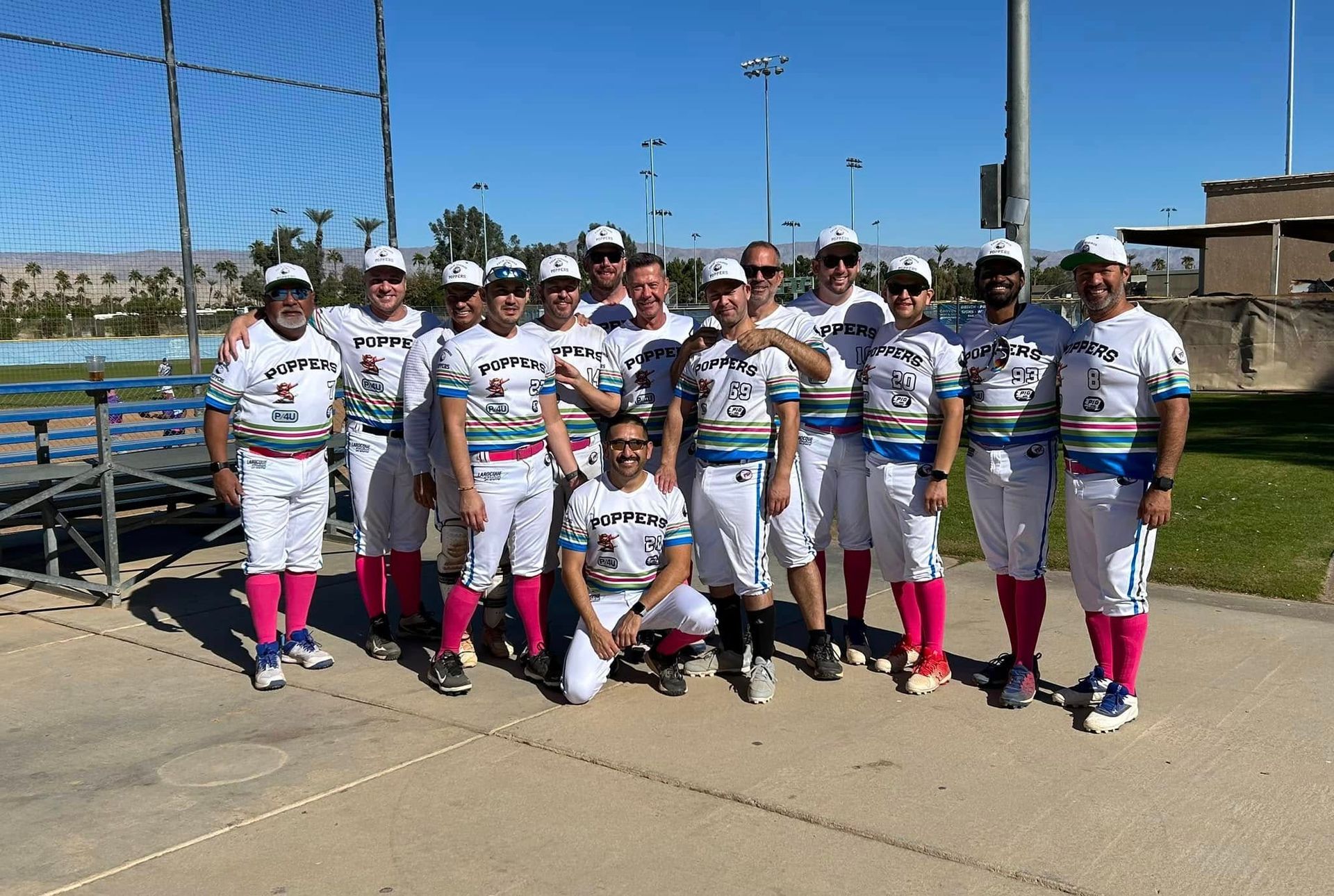 Youth softball team posing on a sunny field, wearing white uniforms with pink socks