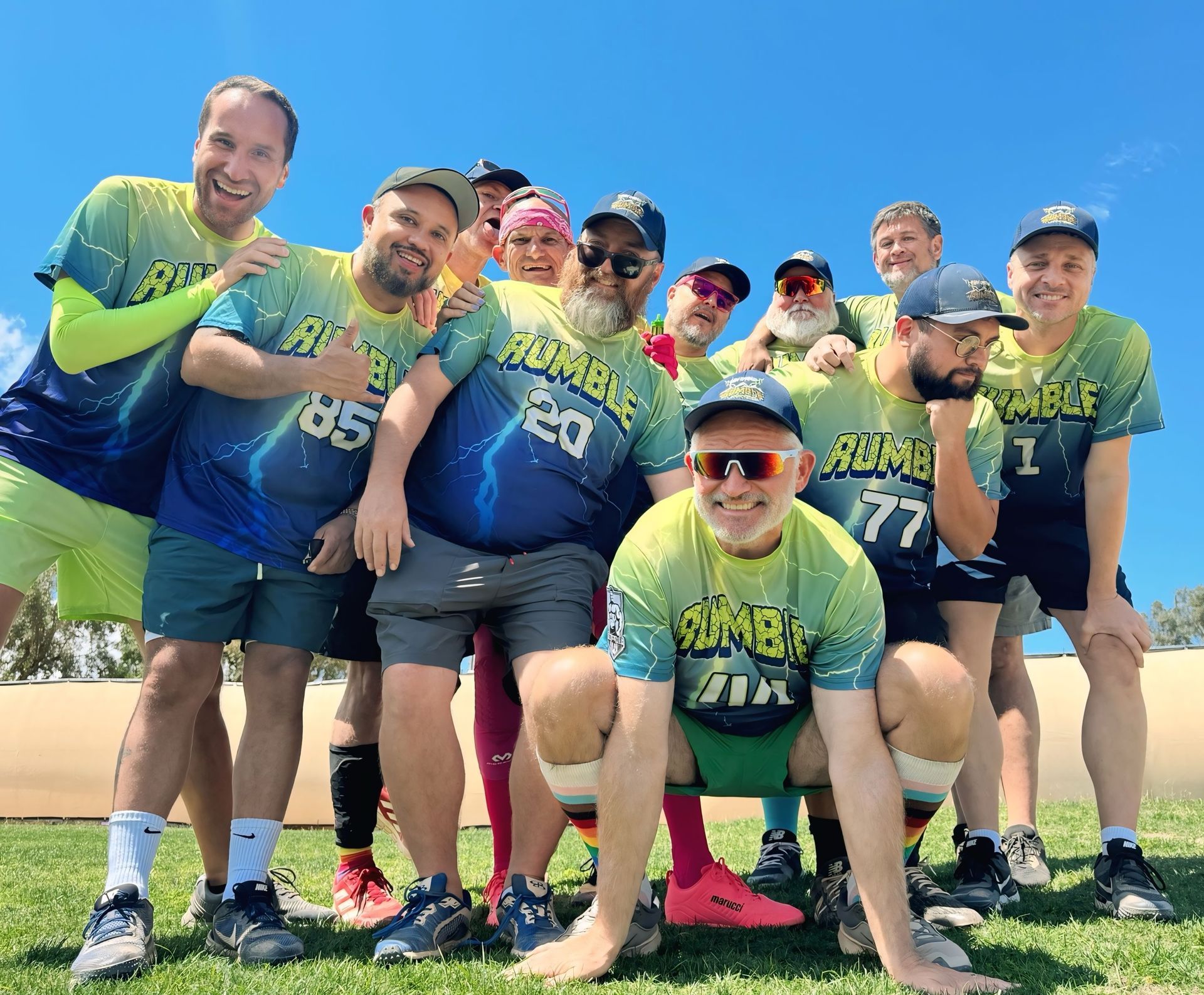Group of runners posing together outdoors in colorful shirts after a muddy race, smiling at the camera.
