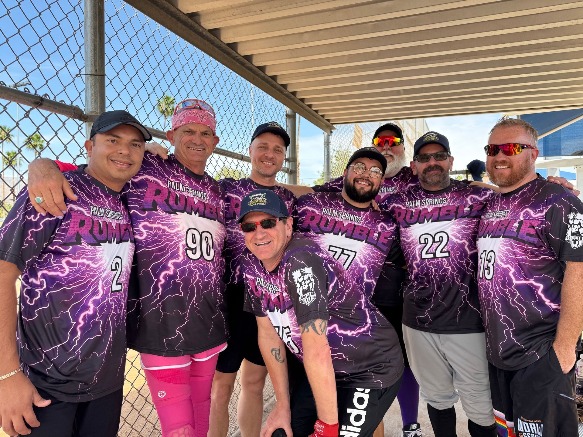 Group of people in purple event jerseys posing outdoors under a pavilion, smiling at the camera.