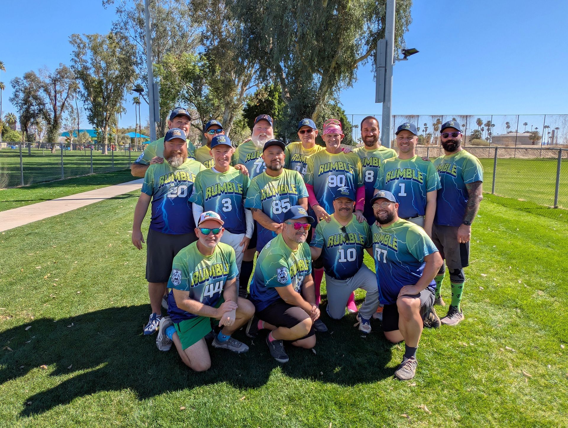 Youth soccer team posing on a sunny field, wearing blue-green jerseys and holding a trophy.