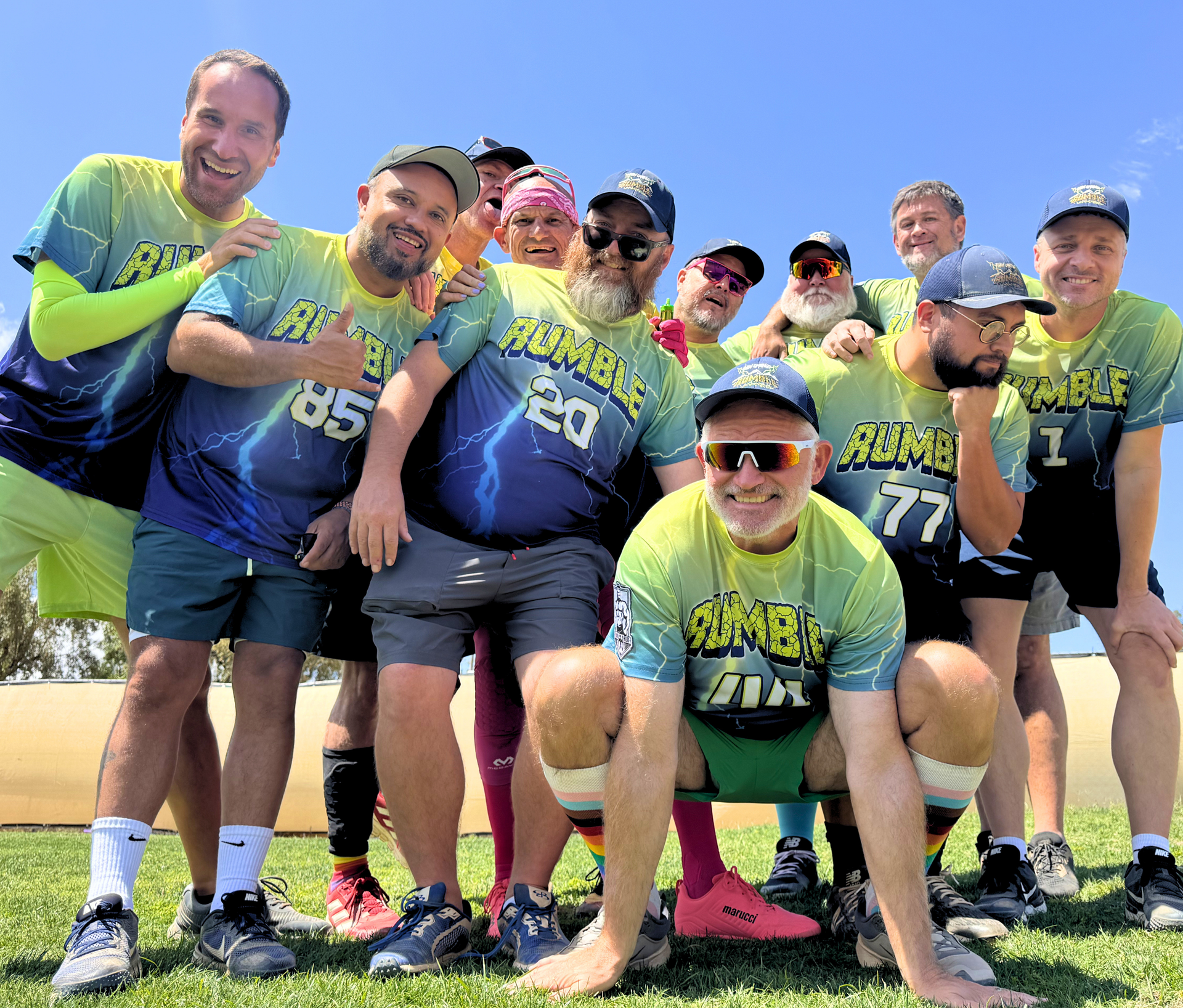 Group of runners in neon jerseys posing outdoors on grass, smiling and crouching together before a race.