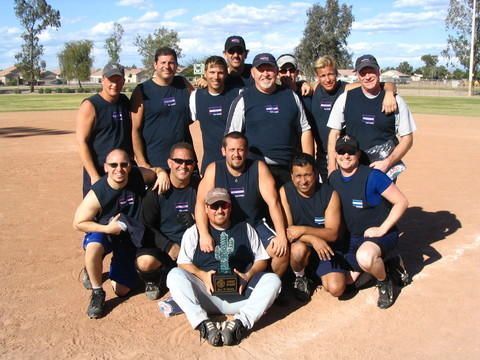 Group of people posing in sports uniforms on a baseball field under a clear sky