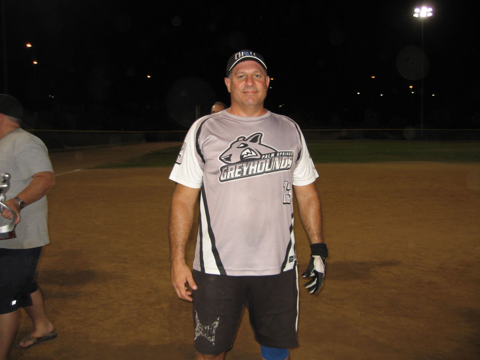 Softball player in neon green jersey stands at home plate, holding a bat ready to swing.