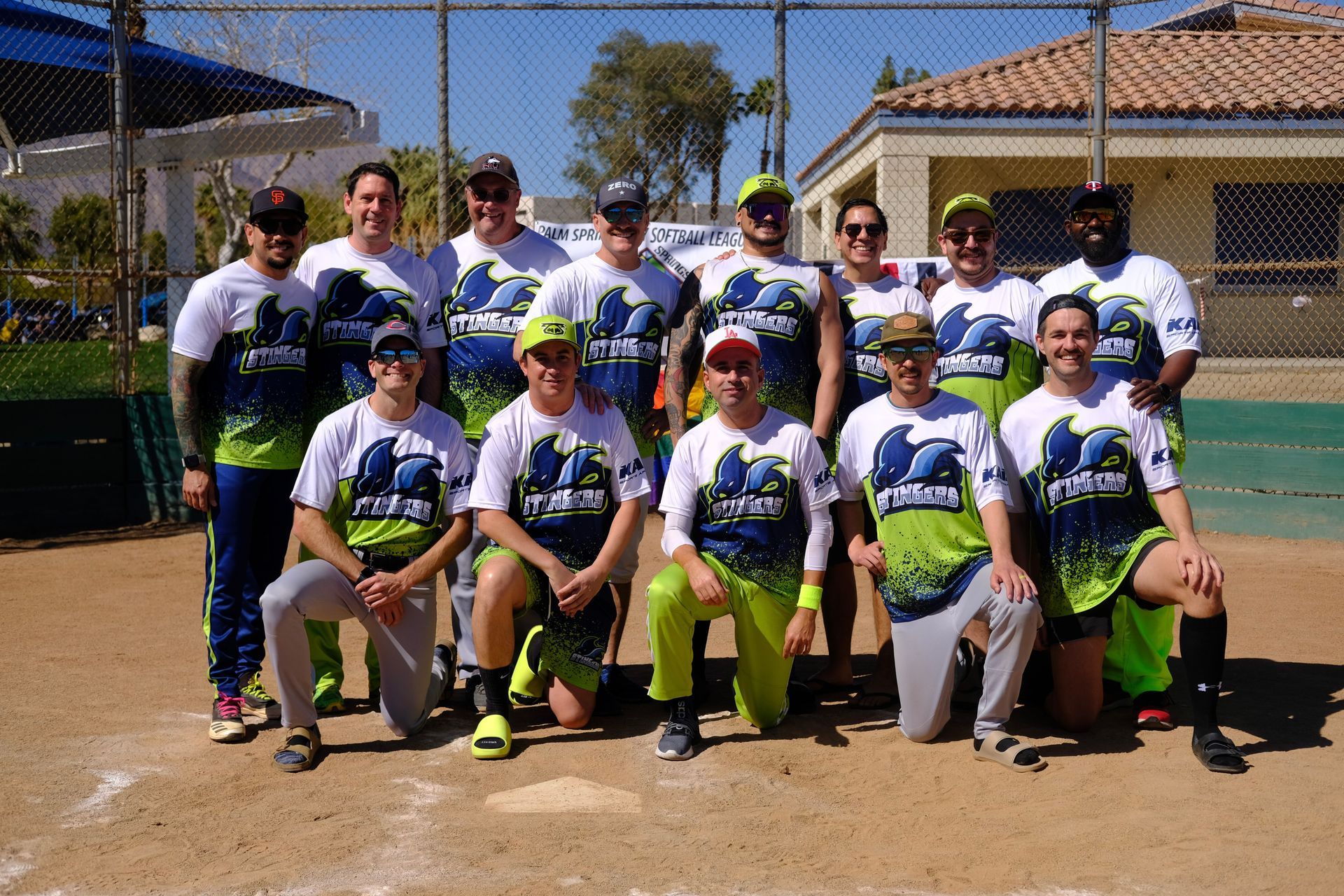 Group of baseball players posing in white and green uniforms on a dirt field