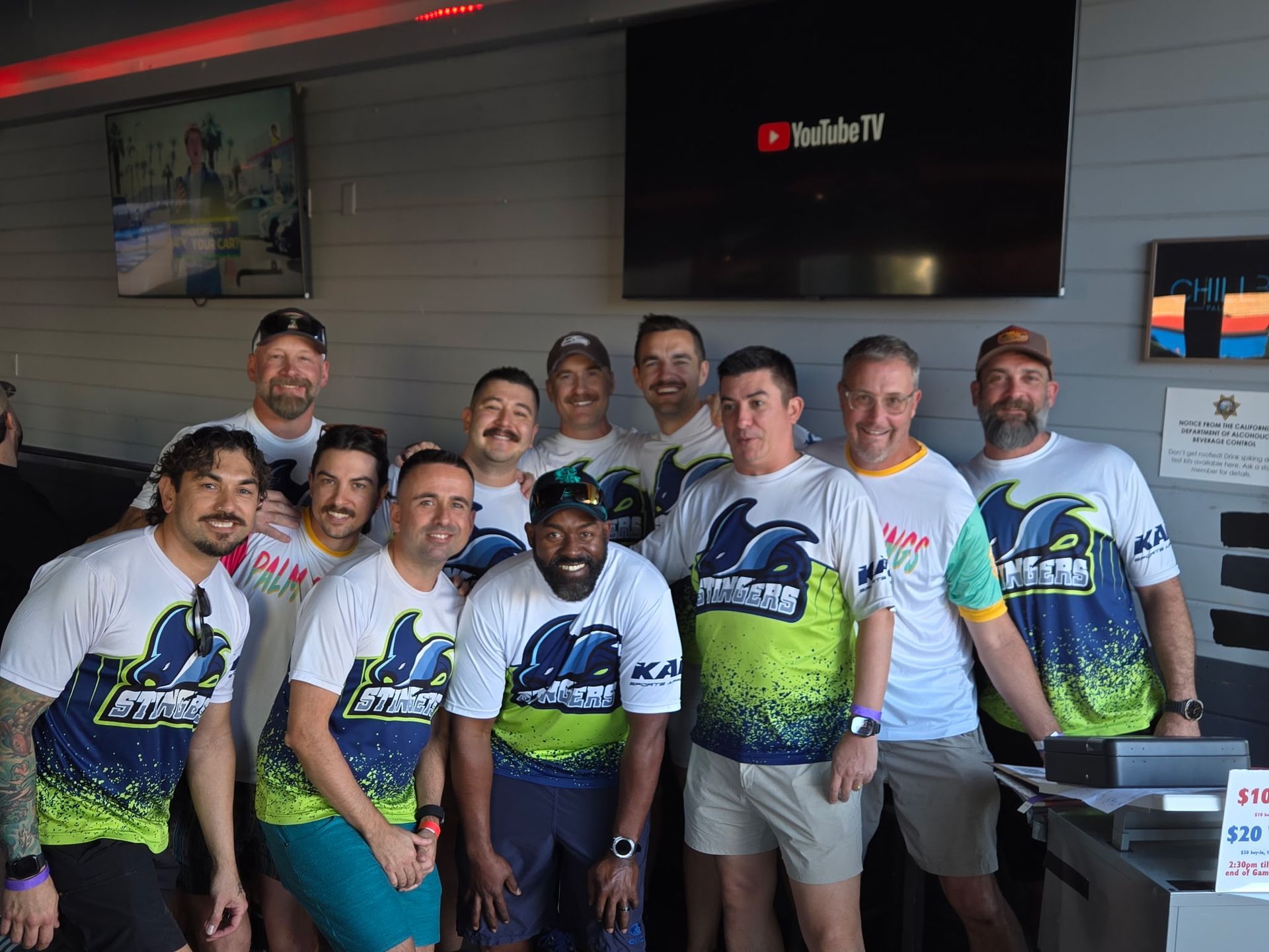 Group of people in matching white and green jerseys posing indoors under a YouTube TV screen