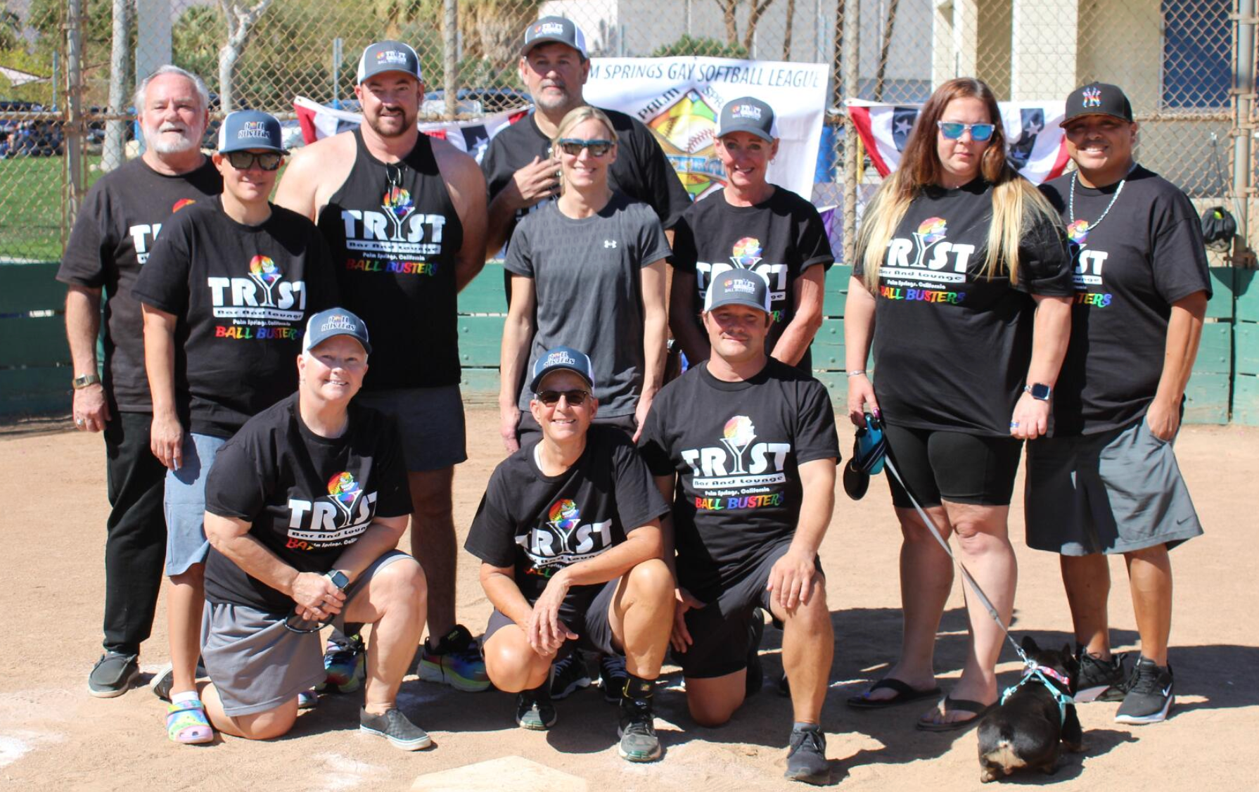 Group of volunteers in matching black T-shirts posing outdoors in front of a fence.