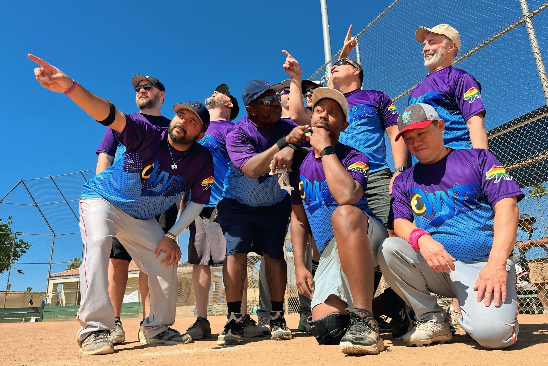 Group of softball players in purple and blue uniforms posing together on a sunny field