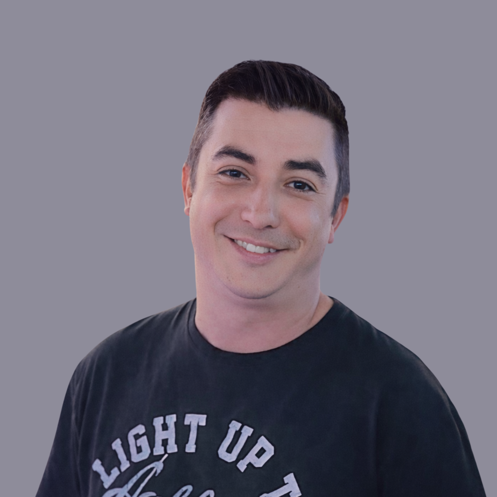 A headshot of Zac Douglas, a man smiling, wearing a black T-shirt, set against a gray background.