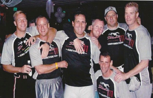 Group of six people in matching black shirts posing together at an indoor event.