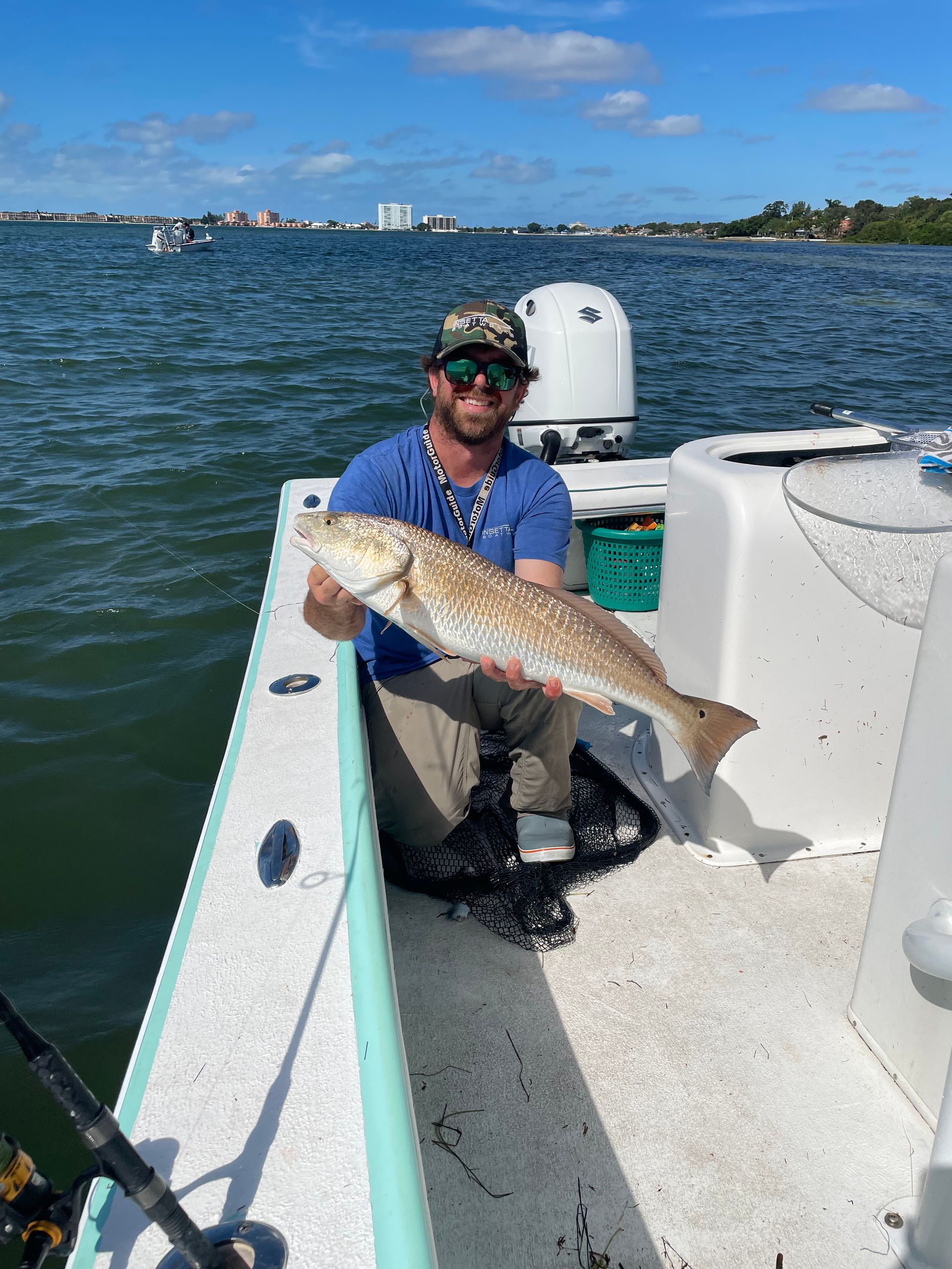 A man is kneeling on a boat holding a large fish.