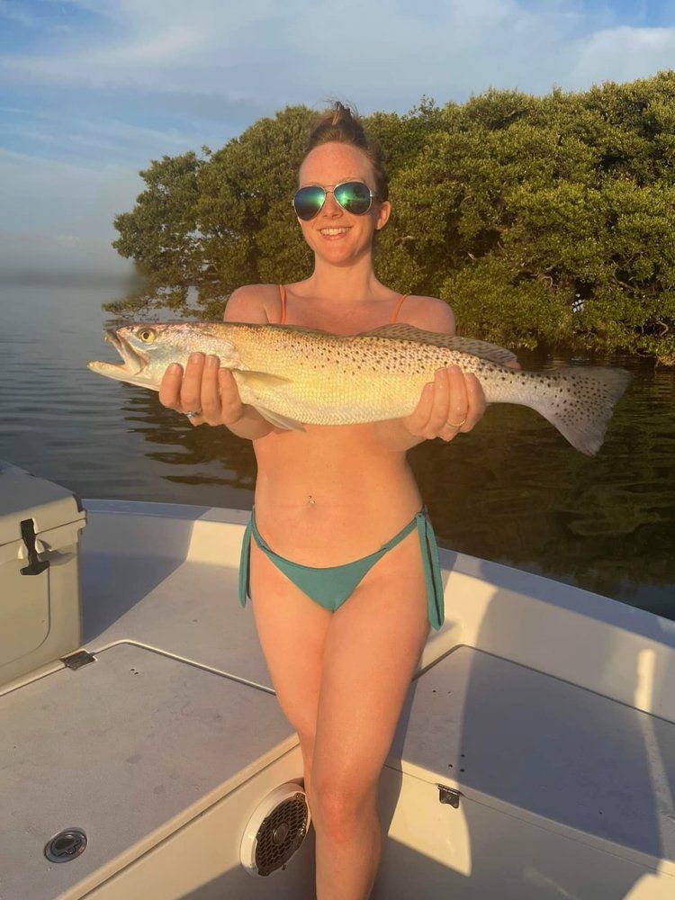 A woman in a bikini is holding a large fish on a boat.