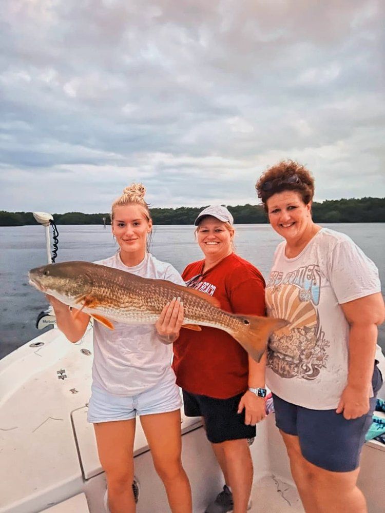 Three women are standing on a boat holding a large fish.